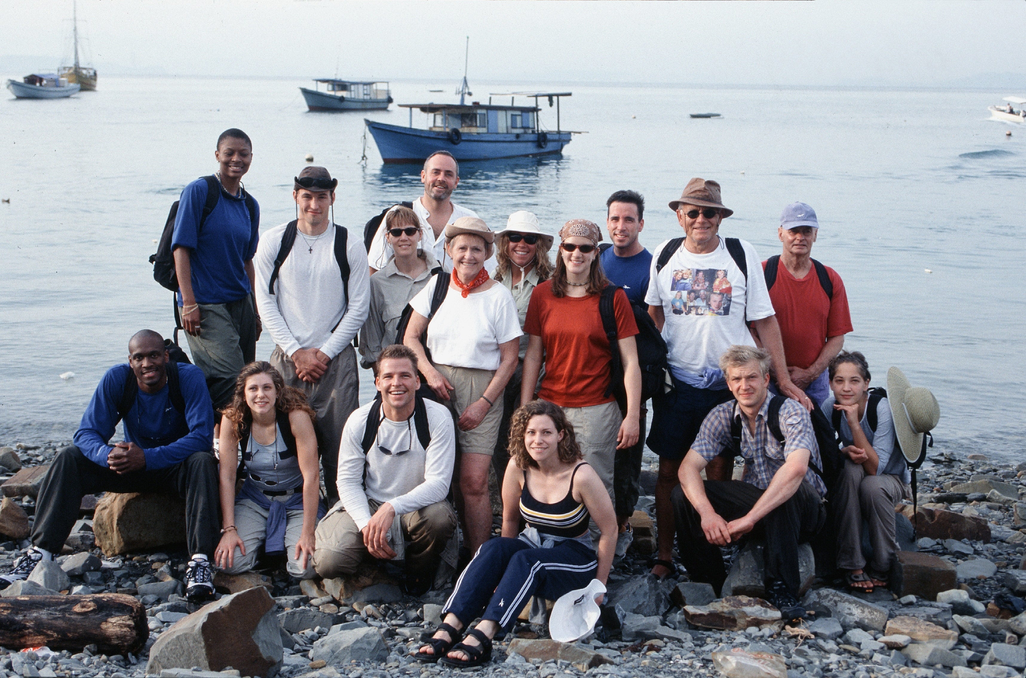 Group of radical   smiling by a rocky shoreline with boats successful  the background, dressed casually for an outdoor excursion