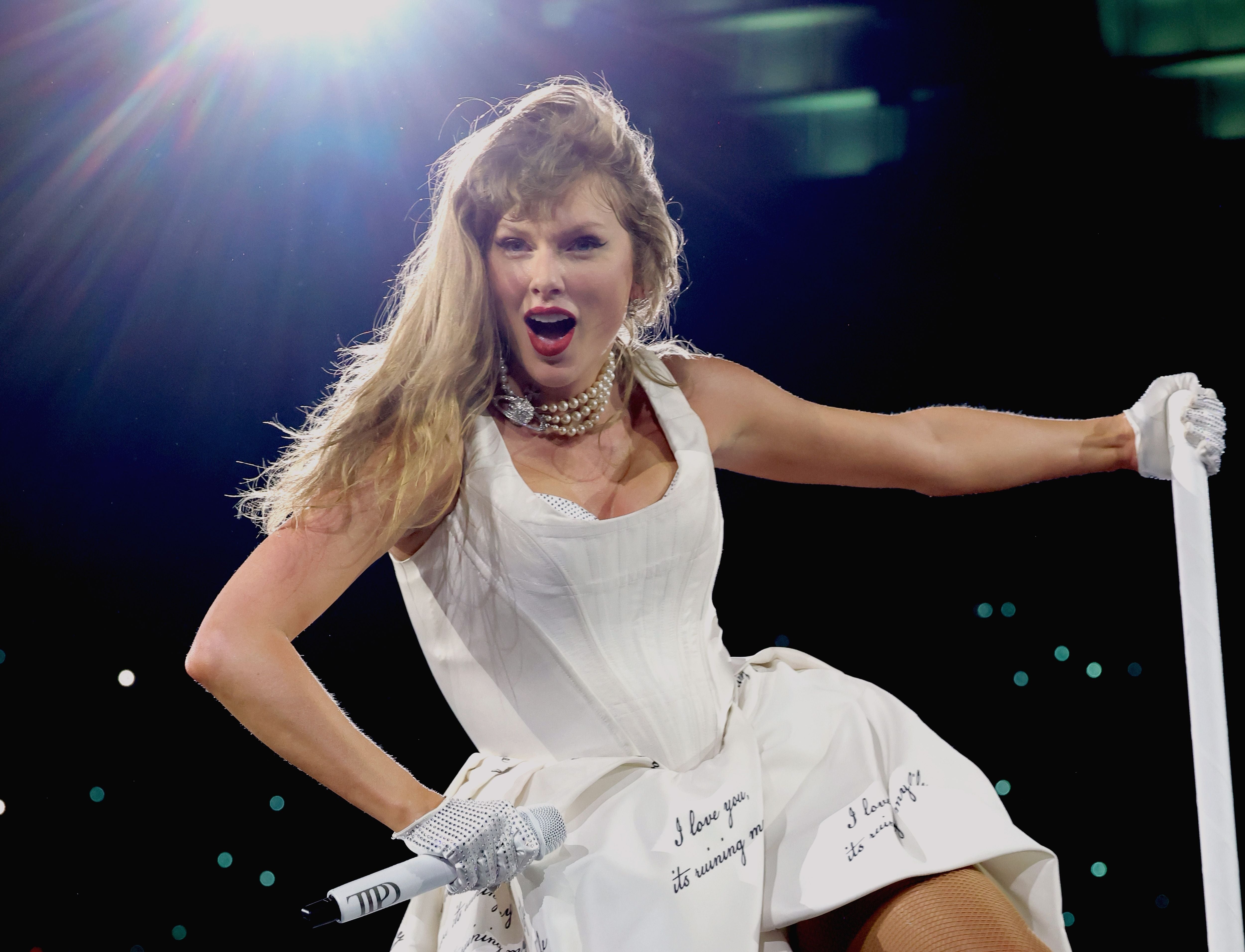 Performer successful a stylish, sleeveless achromatic formal sings energetically connected stage, holding a mic stand, with agleam lights successful the background