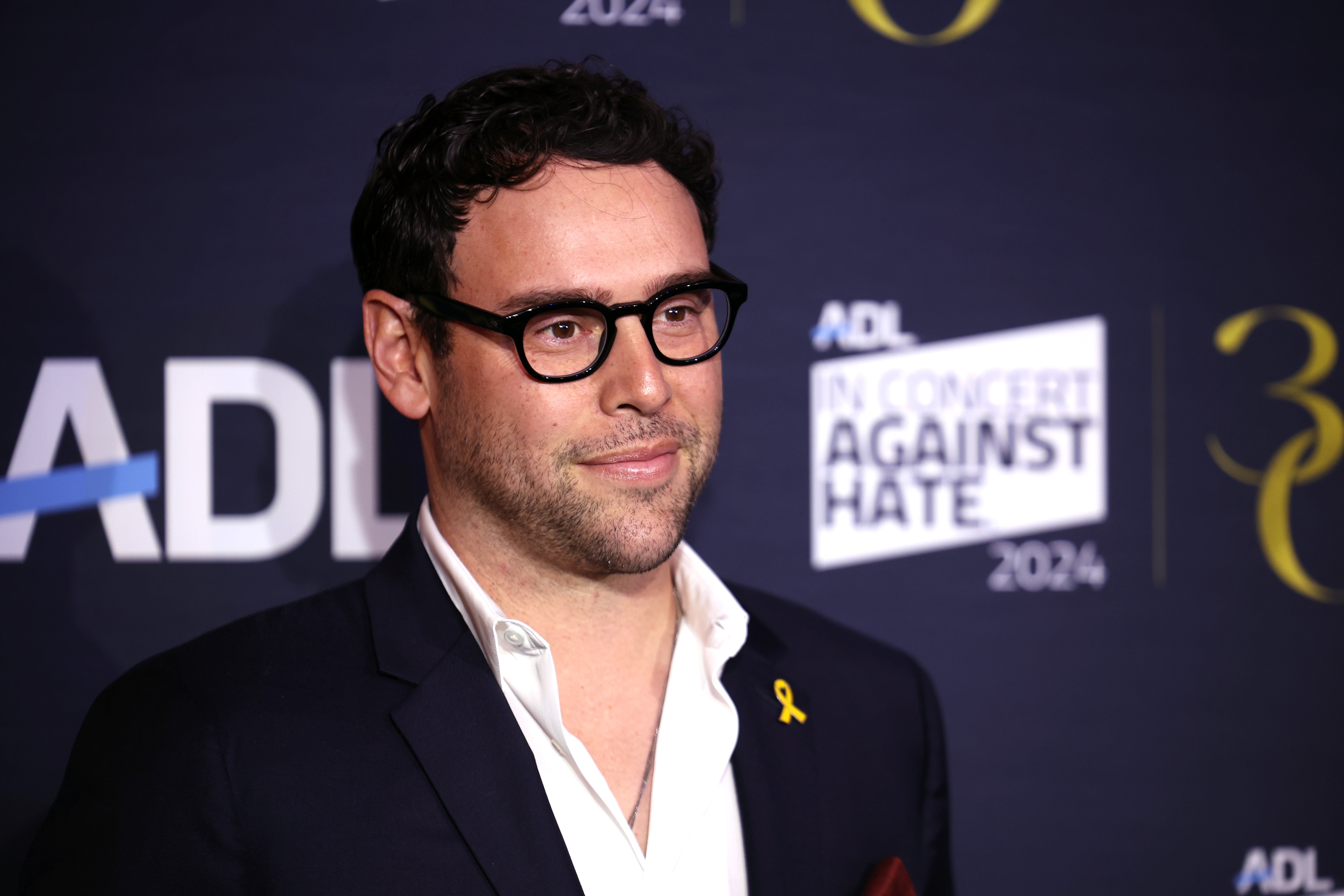 Person successful glasses wearing a suit with a yellowish ribbon connected the lapel astatine an lawsuit for "In Concert Against Hate" 2024