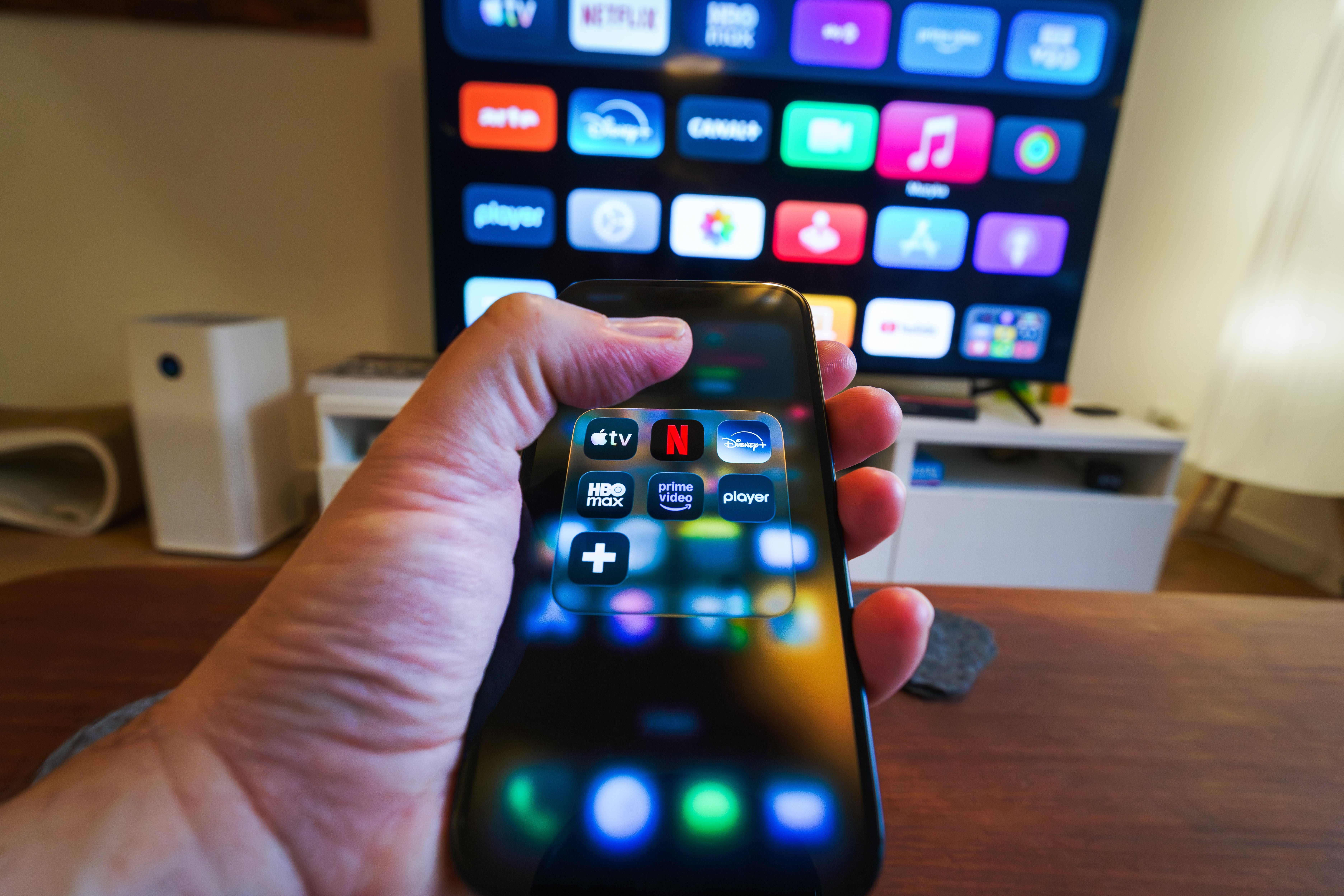 Orang yang memegang remote TV, memilih aplikasi streaming seperti Netflix dan Prime Video di layar TV dalam pengaturan rumah