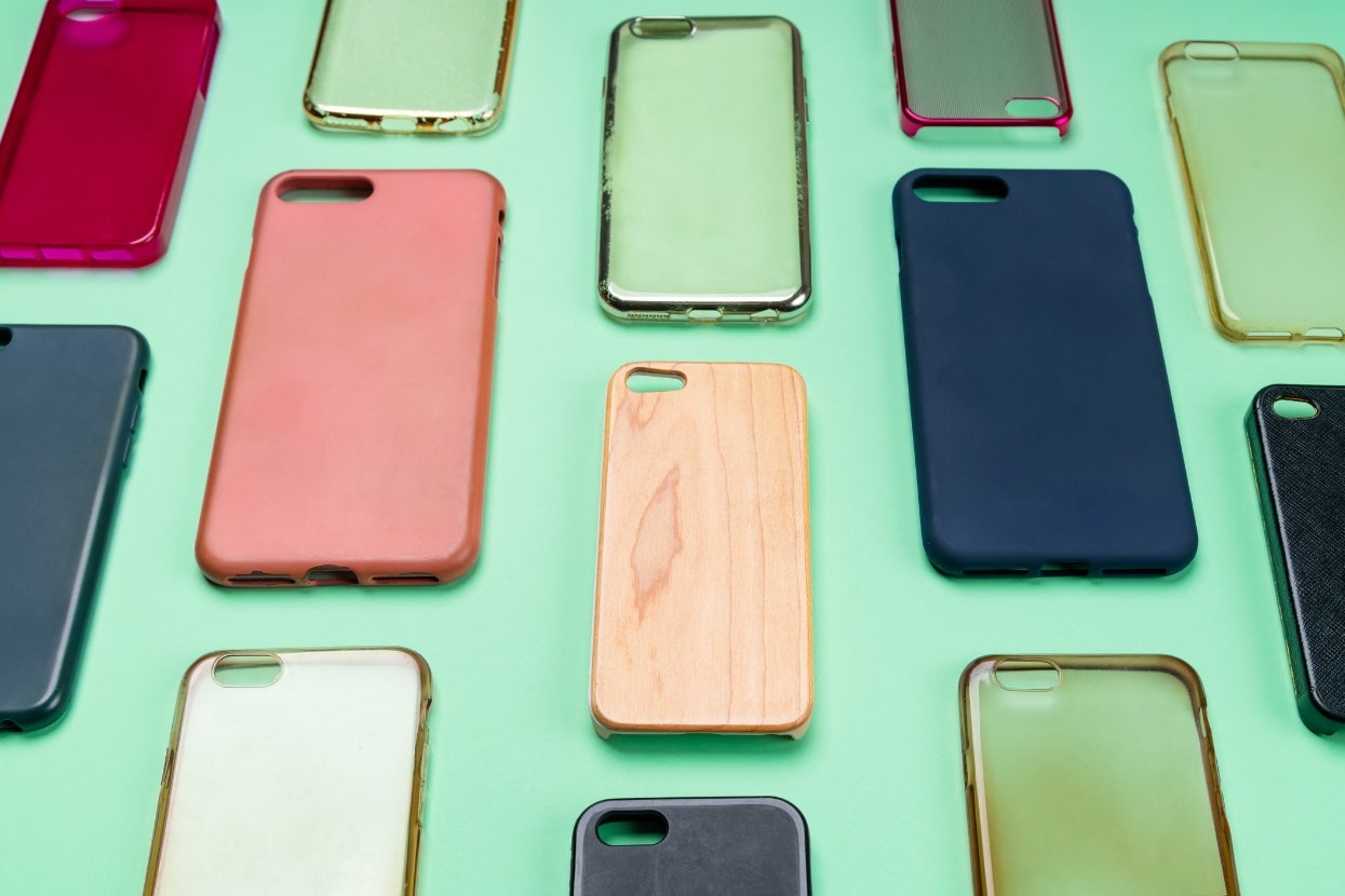 Various smartphone cases arranged on a green background, featuring different designs and materials like wood, rubber, and plastic