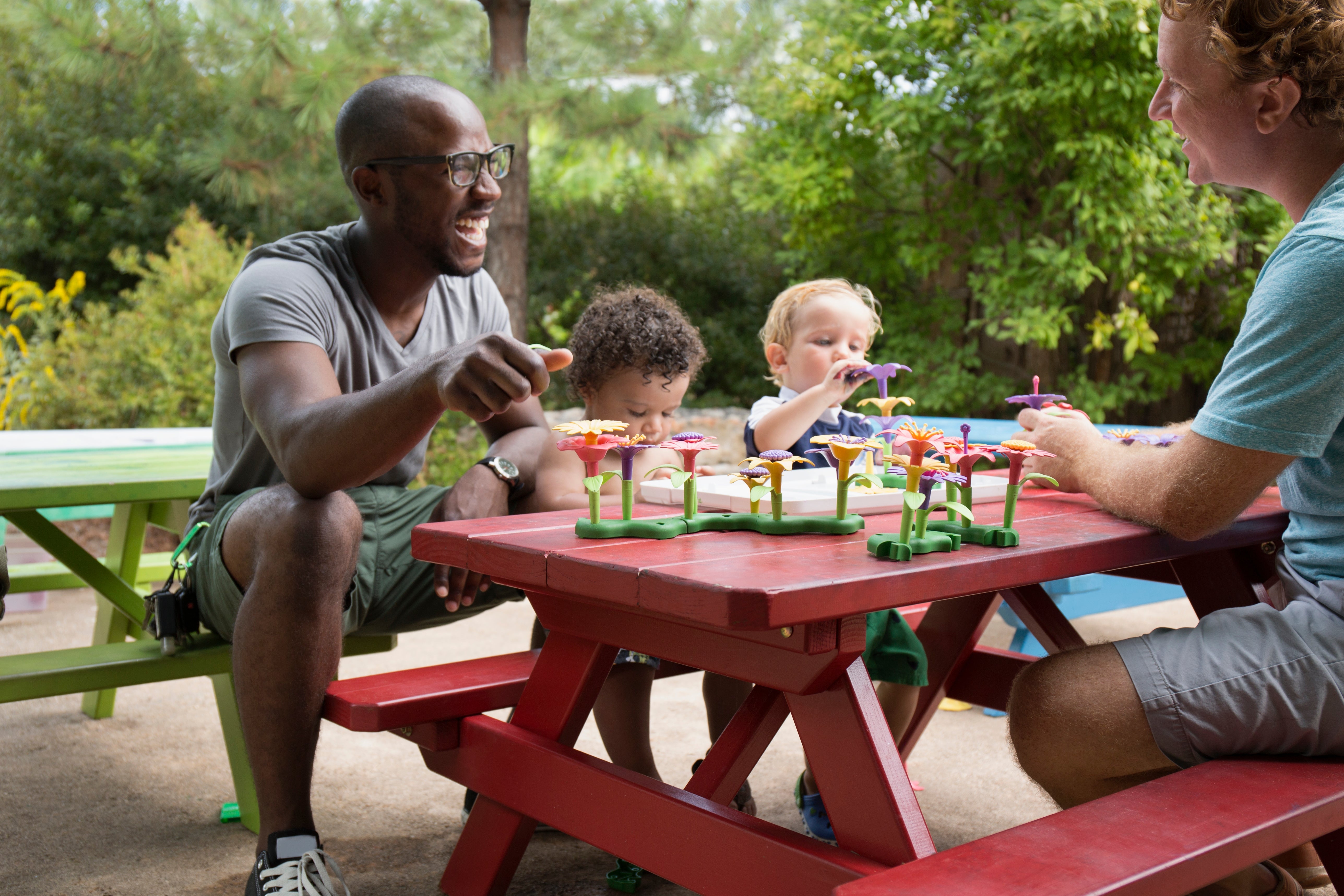 Adults and children happily play with toy flowers at a picnic table in a park setting