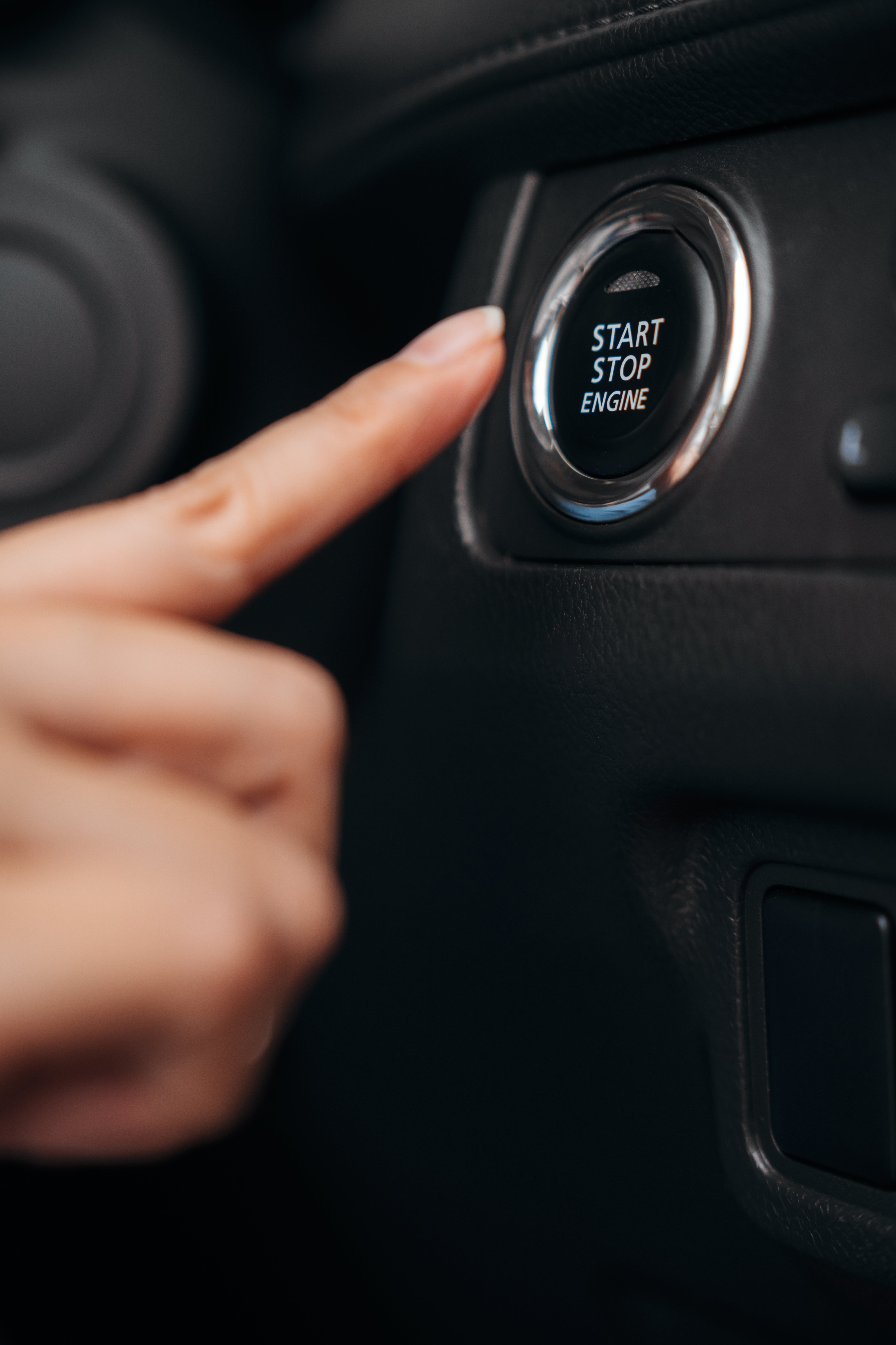 Sebuah tangan terulur untuk menekan tombol start/stop mesin mobil, menyoroti teknologi kendaraan modern