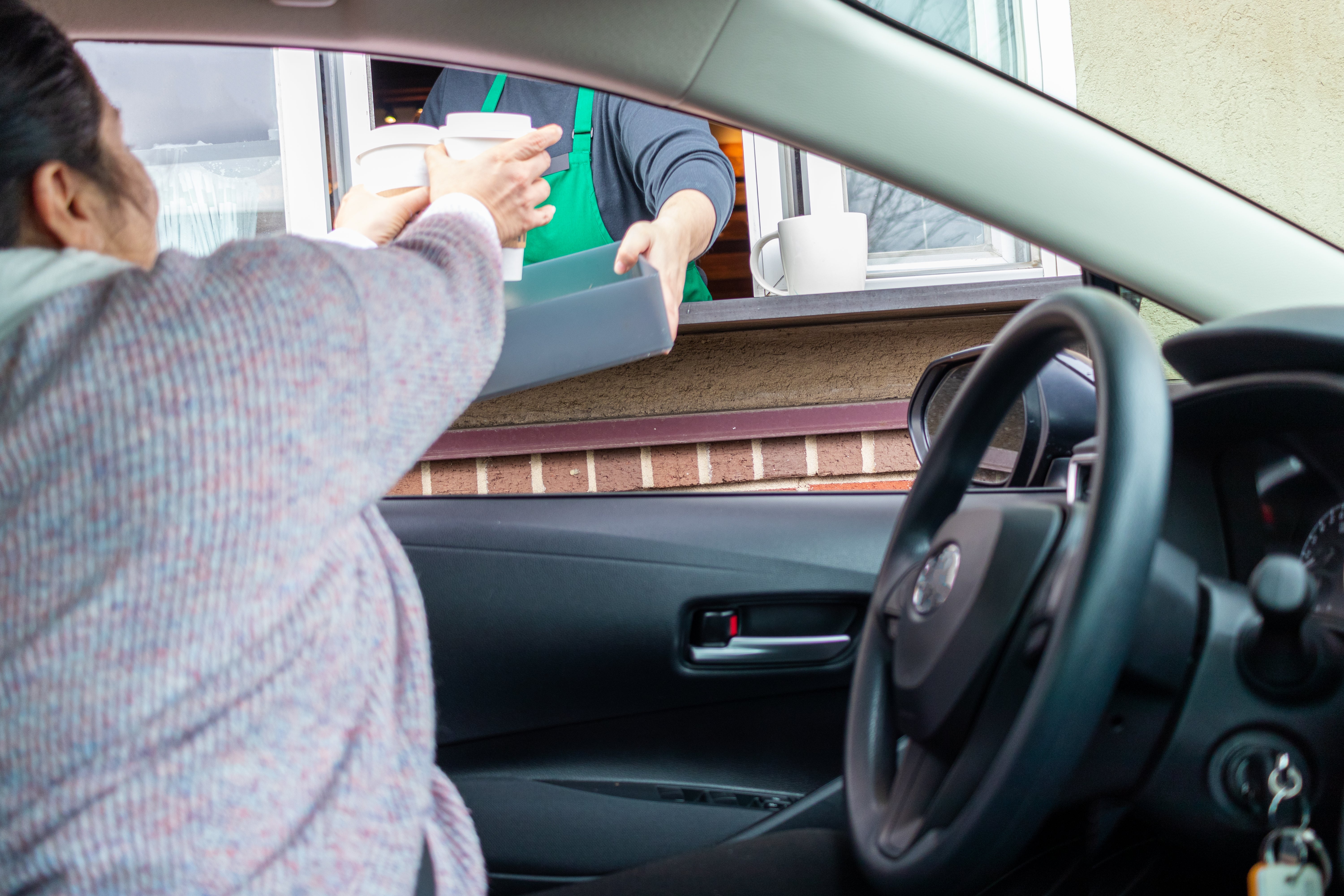 Seseorang di dalam mobil menerima minuman dari barista di jendela drive-thru