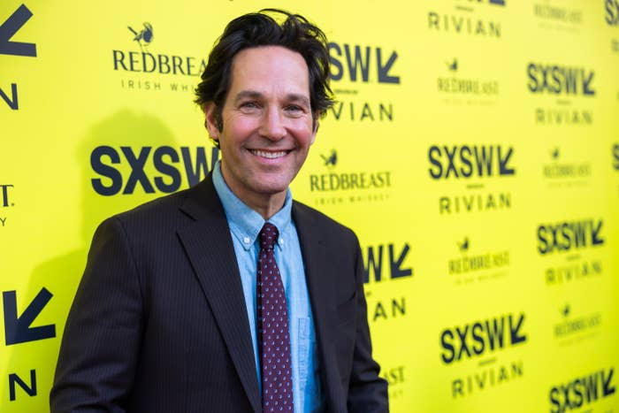 Paul Rudd in a suit and tie smiles at a SXSW event, standing in front of a wall with logos