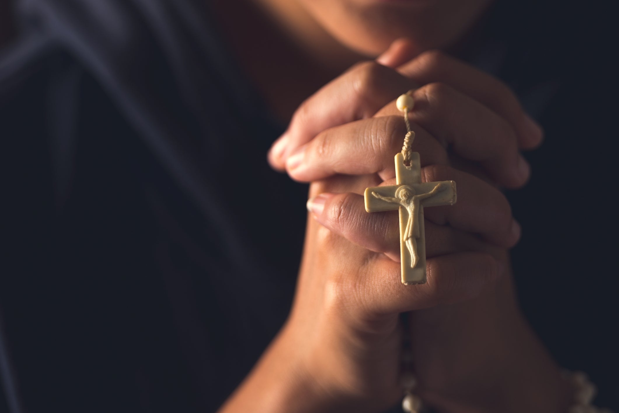 Person holding a rosary and clasped hands in prayer
