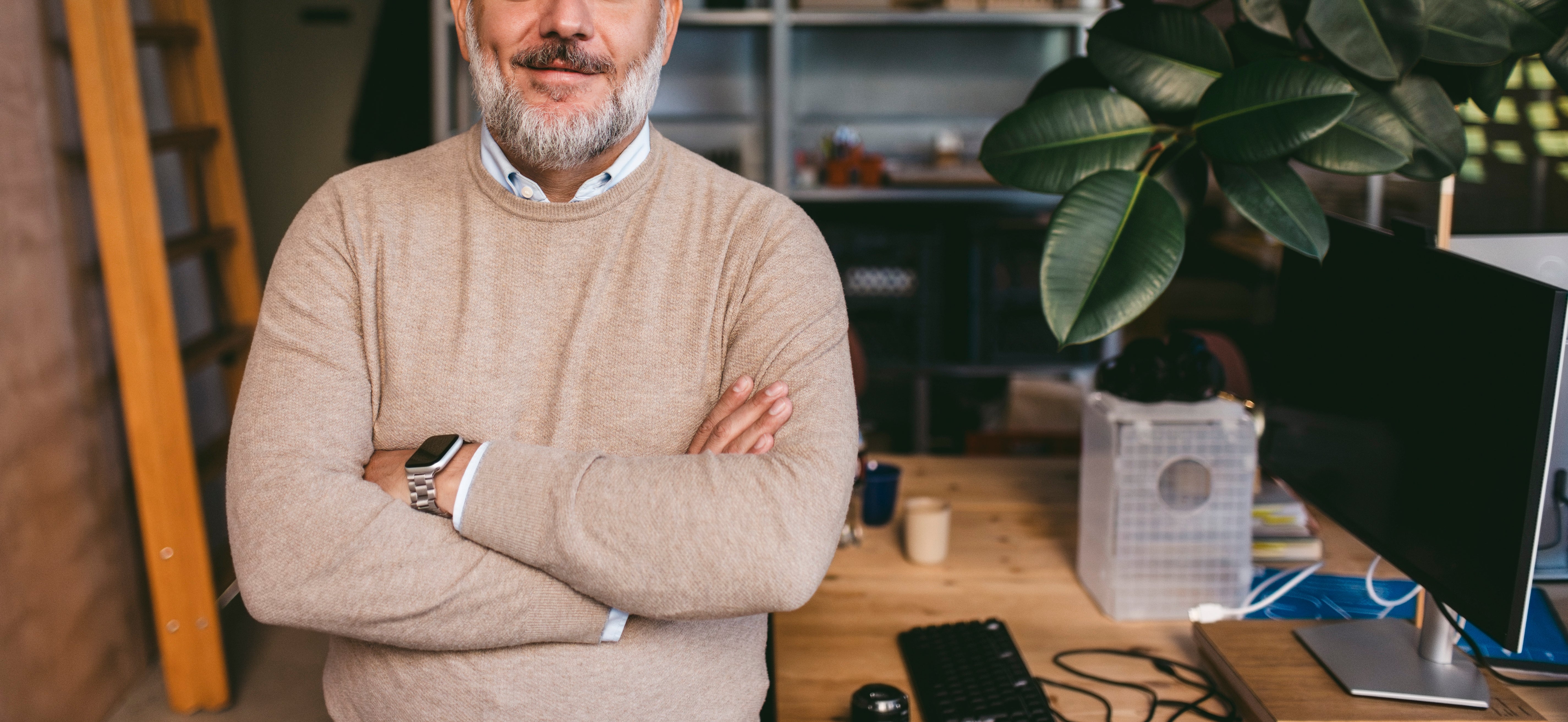 Man with grey hairsbreadth and beard, smiling and lasting with arms crossed successful an bureau environment
