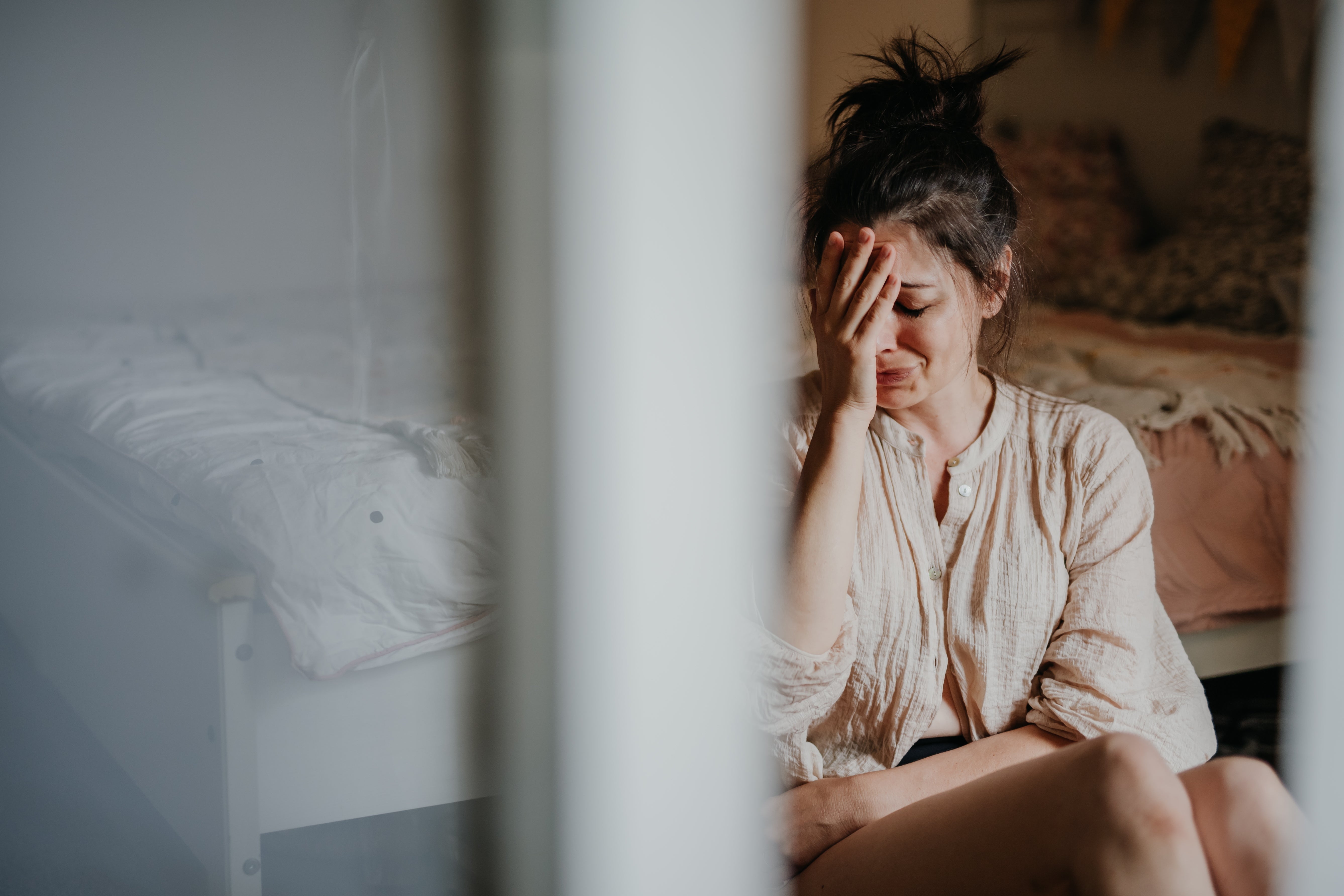 A idiosyncratic sits successful a bedroom, appearing stressed, with manus connected look and eyes closed. The mounting suggests a infinitesimal of affectional reflection