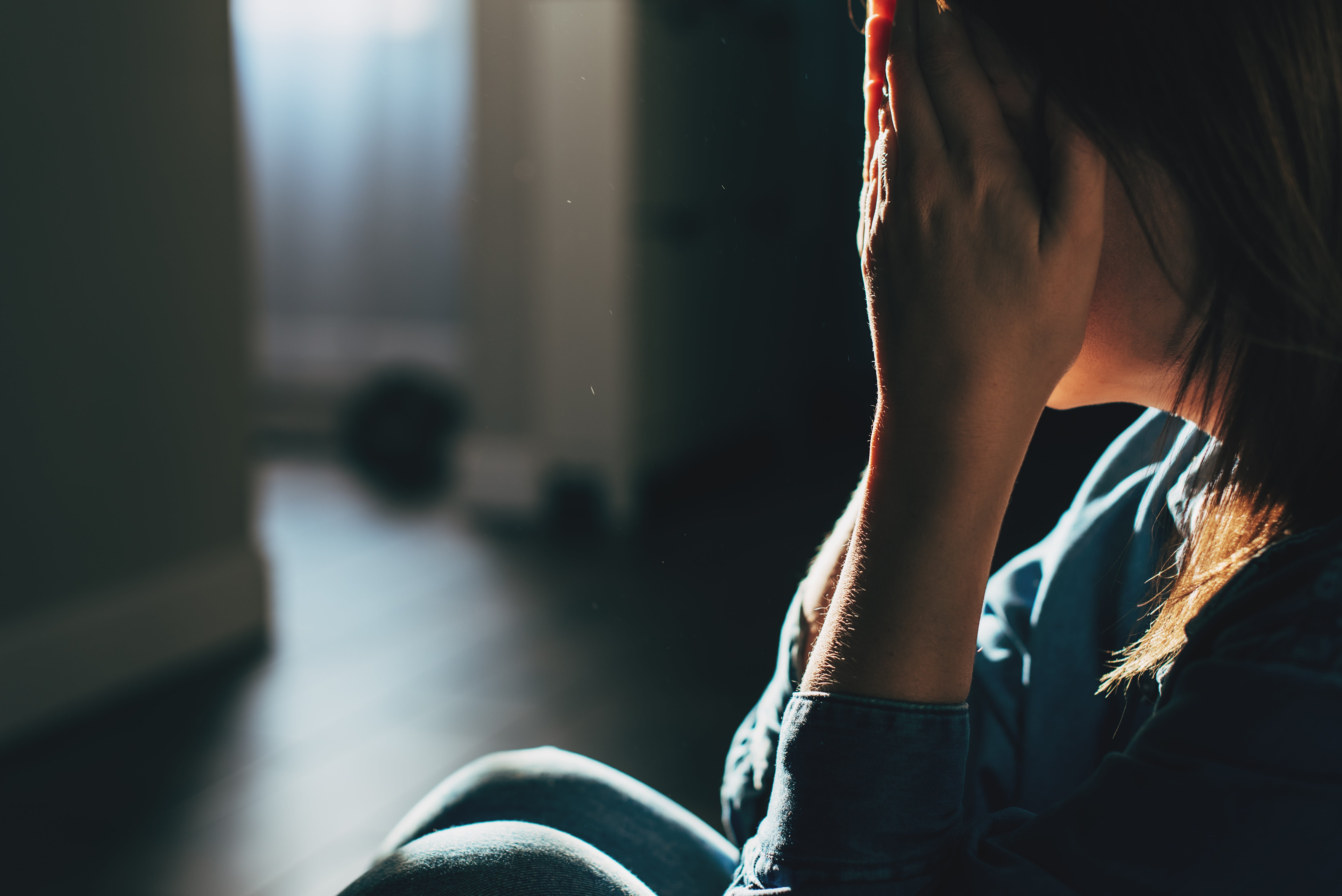 A idiosyncratic sits indoors with hands covering their face, conveying distress oregon heavy thought. The mounting is dimly lit, suggesting an introspective mood