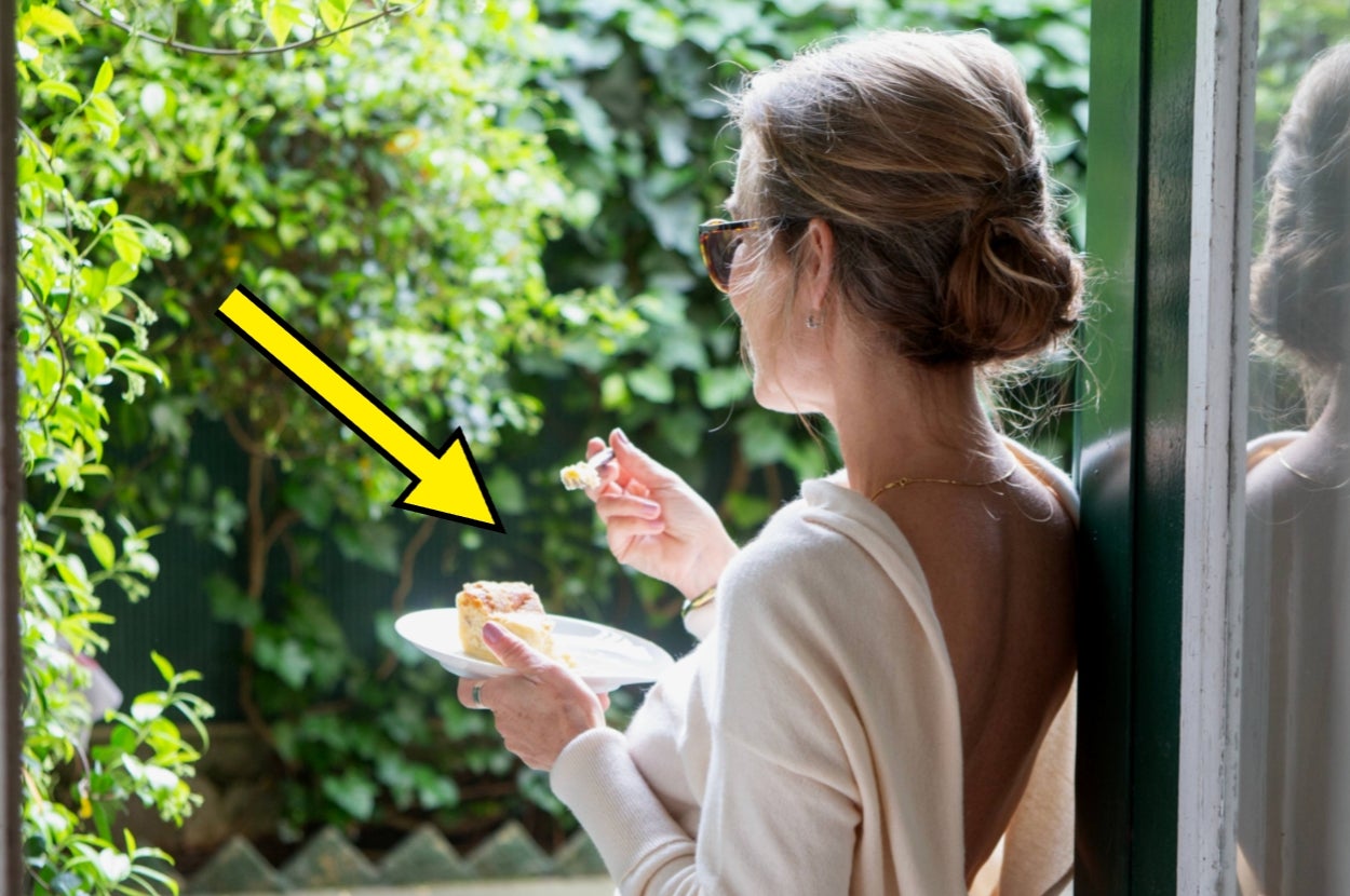 Woman enjoying a piece of cake in an outdoor setting, wearing sunglasses and a light sweater
