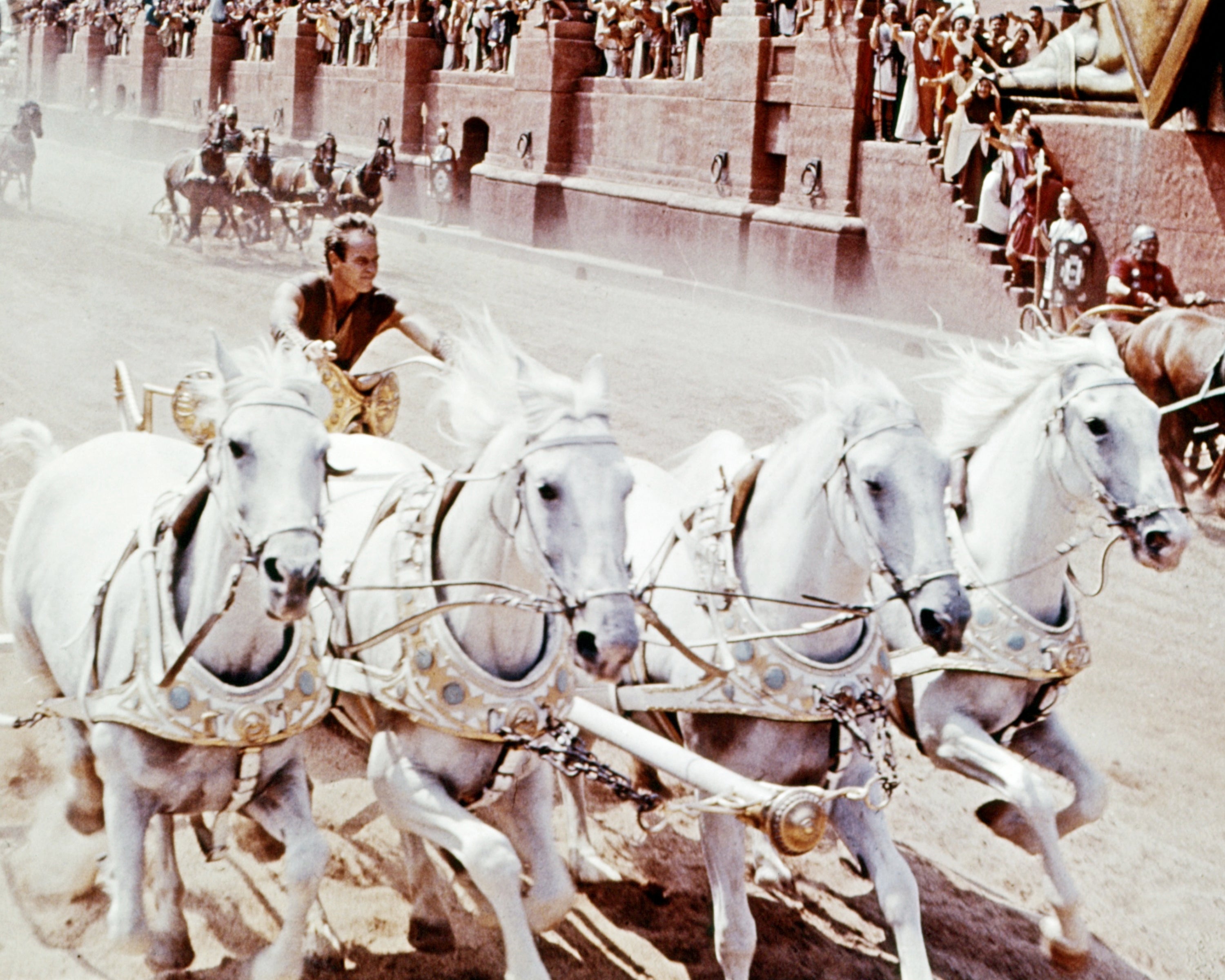 Man driving a chariot pulled by 4 horses successful an past arena scene, surrounded by spectators