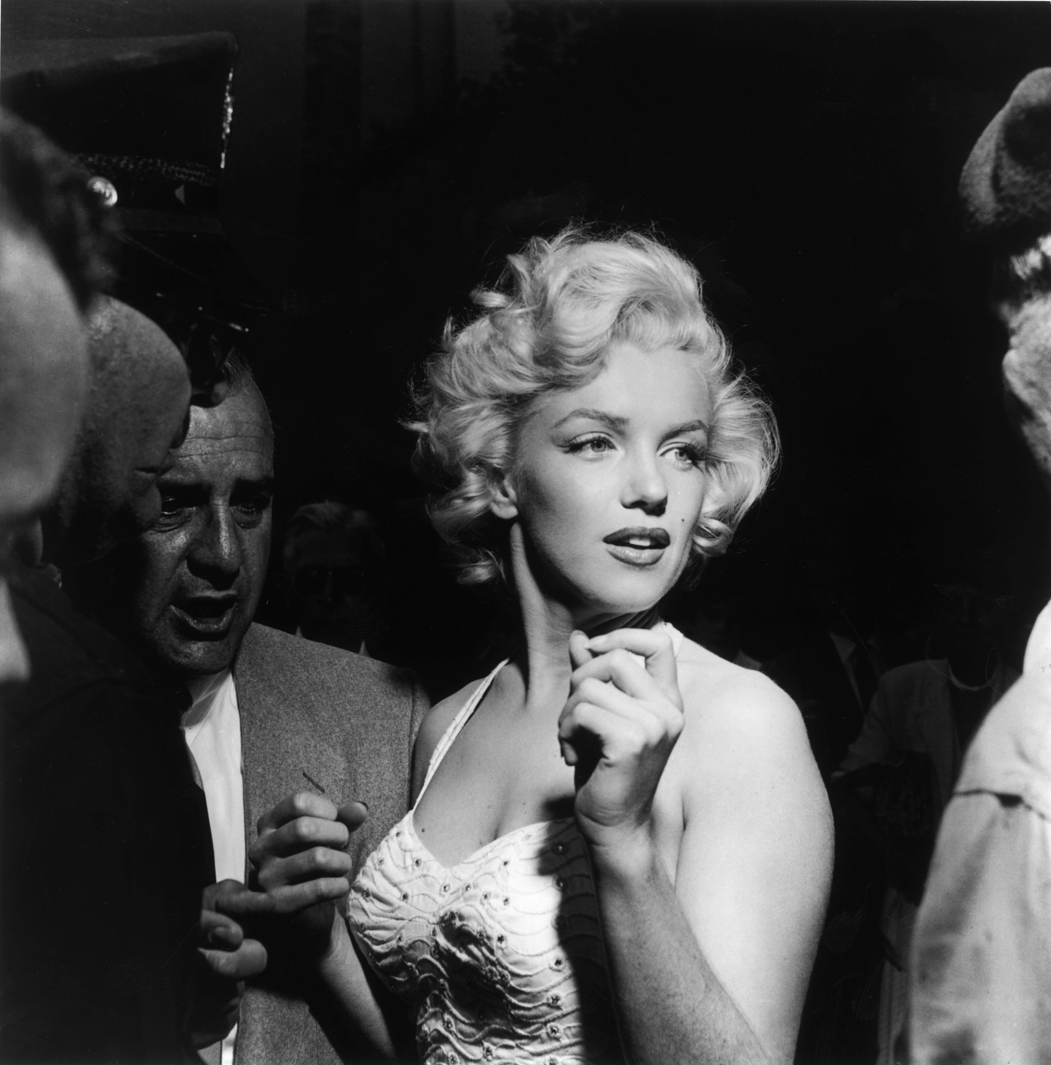 A pistillate with curly hairsbreadth wearing a elaborate formal is surrounded by people, looking disconnected to the side
