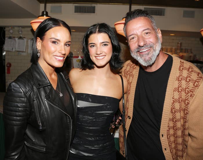 Heidi D'Amelio in a leather jacket, Charli D'Amelio in a strapless dress, and Marc D'Amelio in a sweater huddled together at an event
