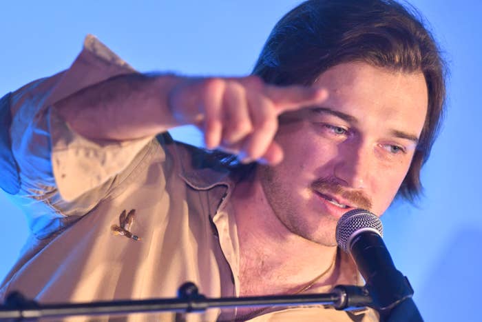 Morgan Wallen speaking into a microphone, gesturing with hand, wearing a casual shirt