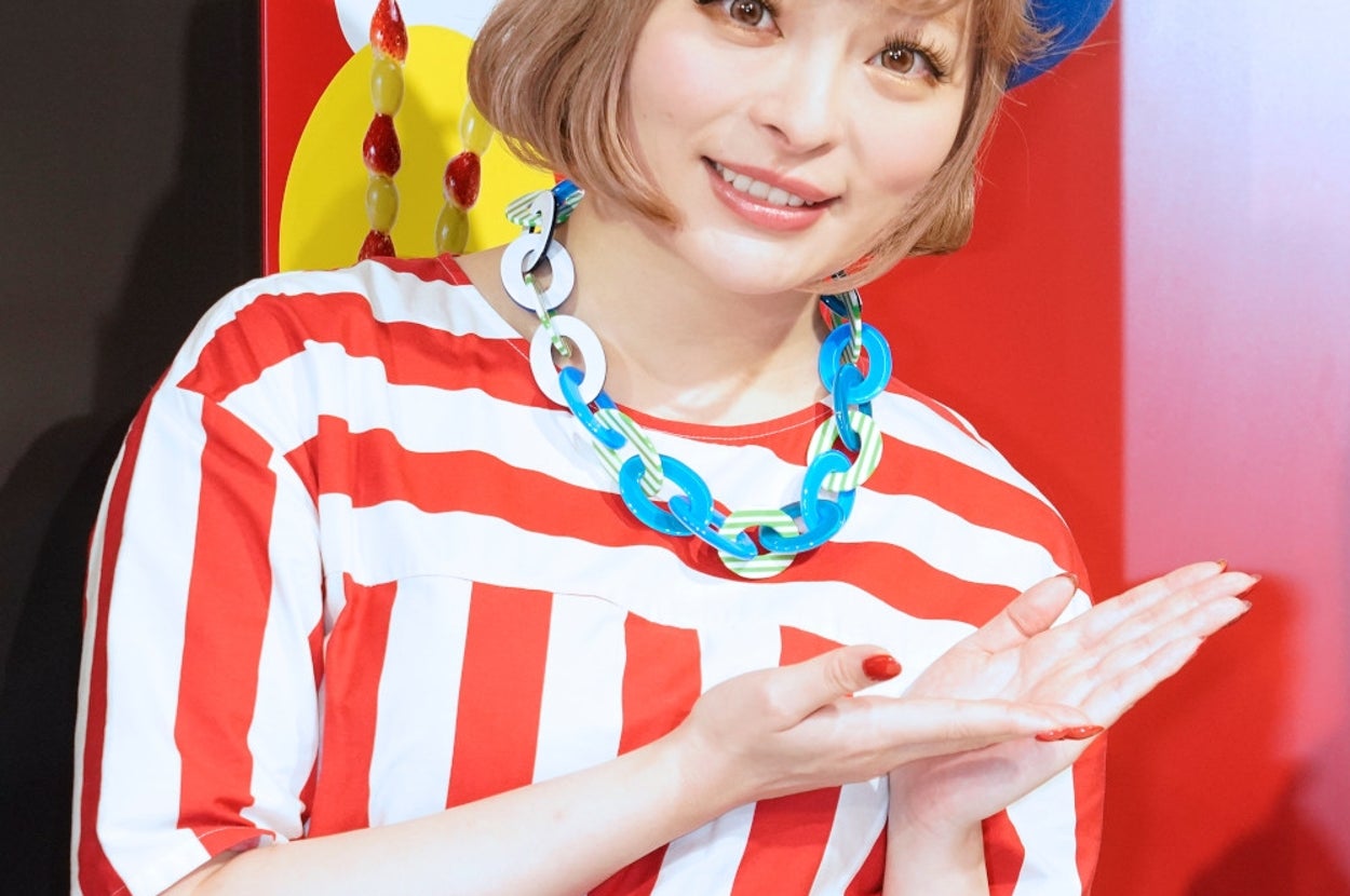 ボーダー柄のトップとベレー帽をかぶった女性がポーズを取る。カラフルなアクセサリーを身に着けている。