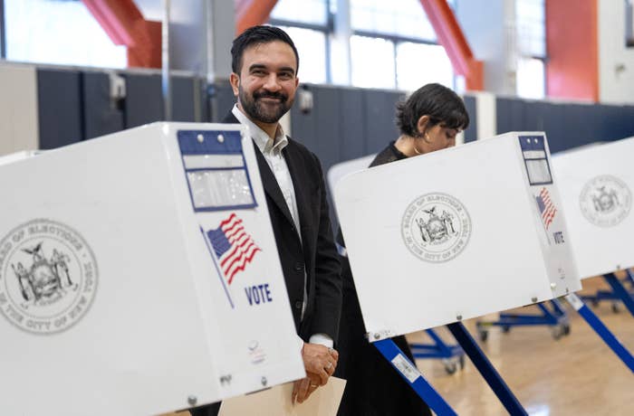 A idiosyncratic   smiling astatine  a voting booth, portion    different  idiosyncratic   adjacent    focuses connected  casting their ballot  astatine  a nationalist   polling location