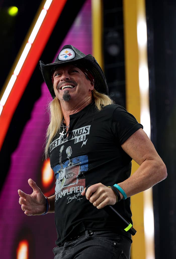 Musician wearing a graphic T-shirt and cowboy hat, smiling onstage during a performance