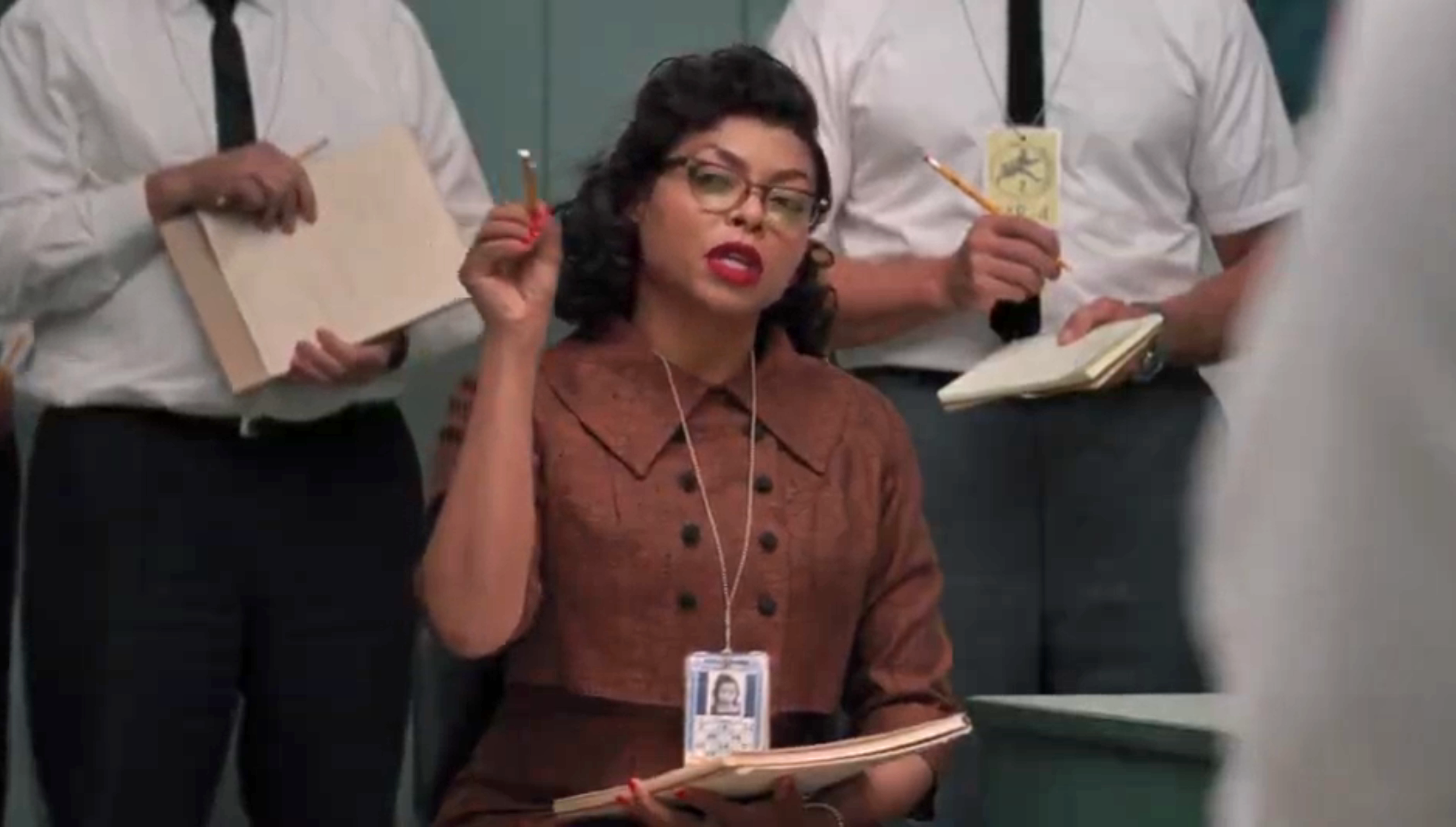A woman in vintage attire holds a pencil and notebook, surrounded by men with notebooks, in an office setting