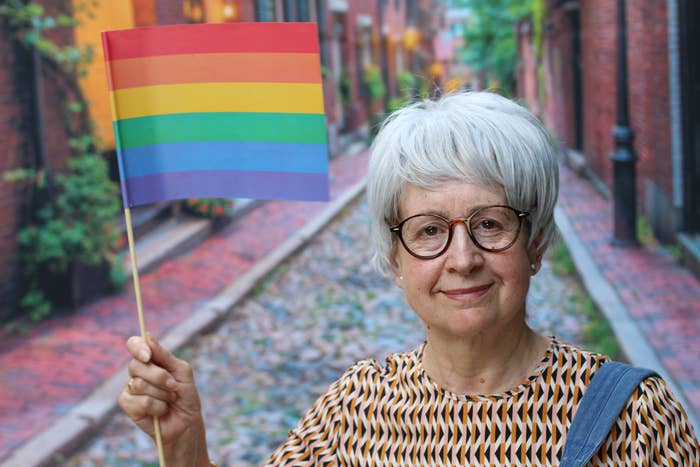 Person with abbreviated  grey  hairsbreadth  and glasses holds a tiny  rainbow flag, lasting  connected  a cobblestone thoroughfare  alley