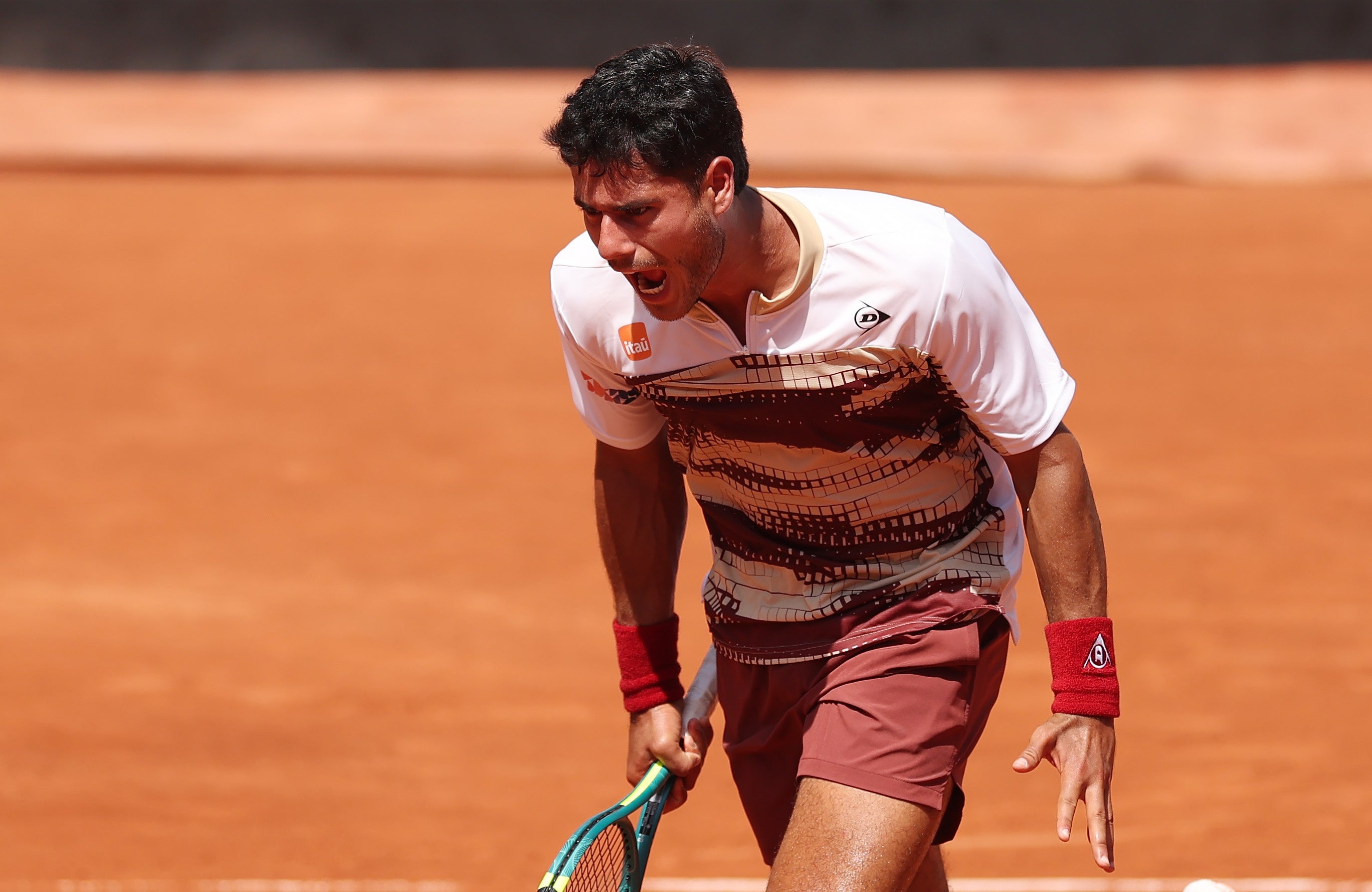 Tennisspiller feirer intenst på en leirebane, iført en skjorte med dynamisk mønster og shorts med armbånd og holder en racket