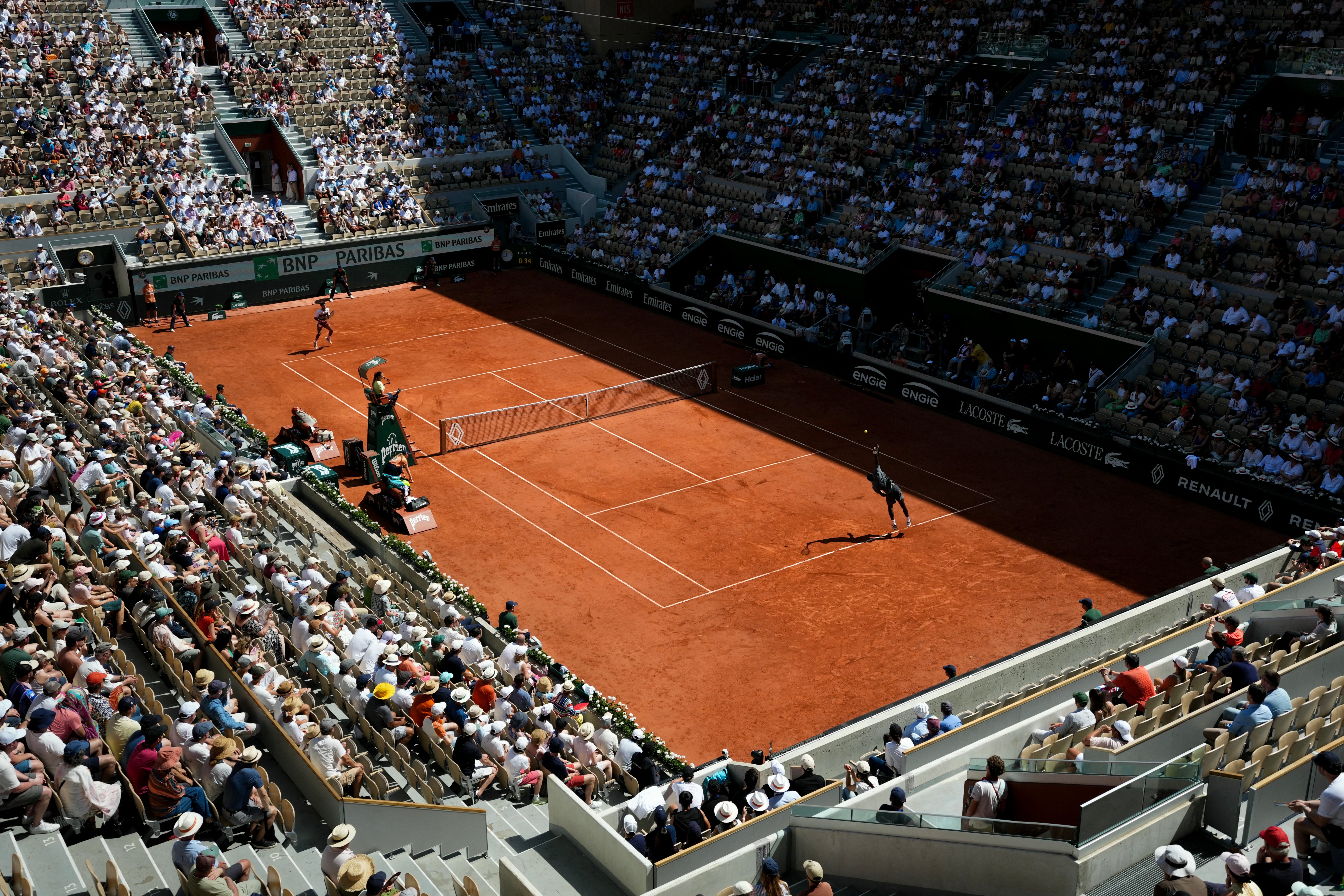 En tenniskamp spilles på en leirbane på et fylt stadion, med tilskuere som følger nøye med på handlingen