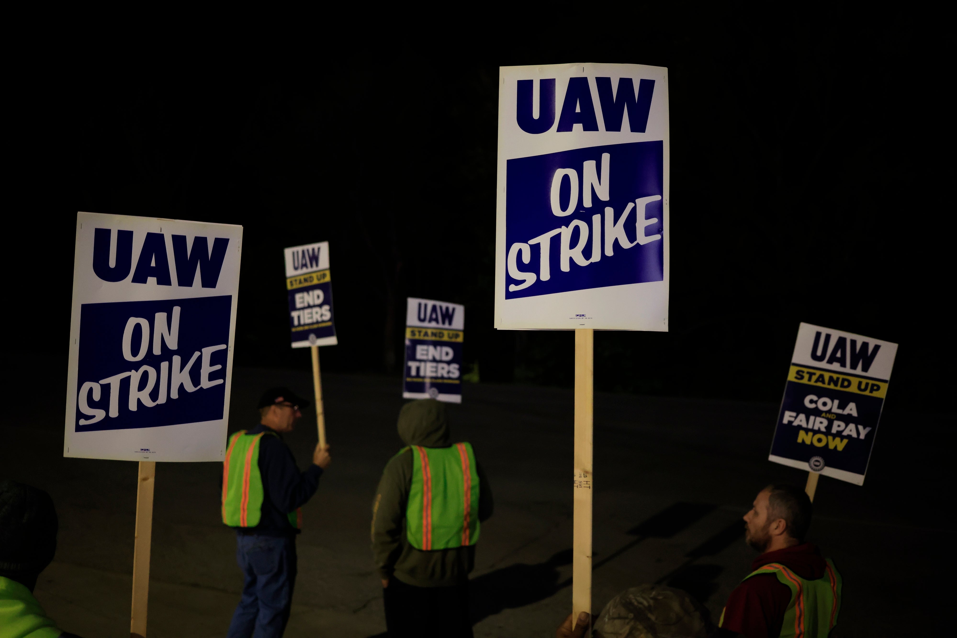 People holding "UAW On Strike" signs astatine  night, advocating for just  wage  and ending tiers during a labour  protest