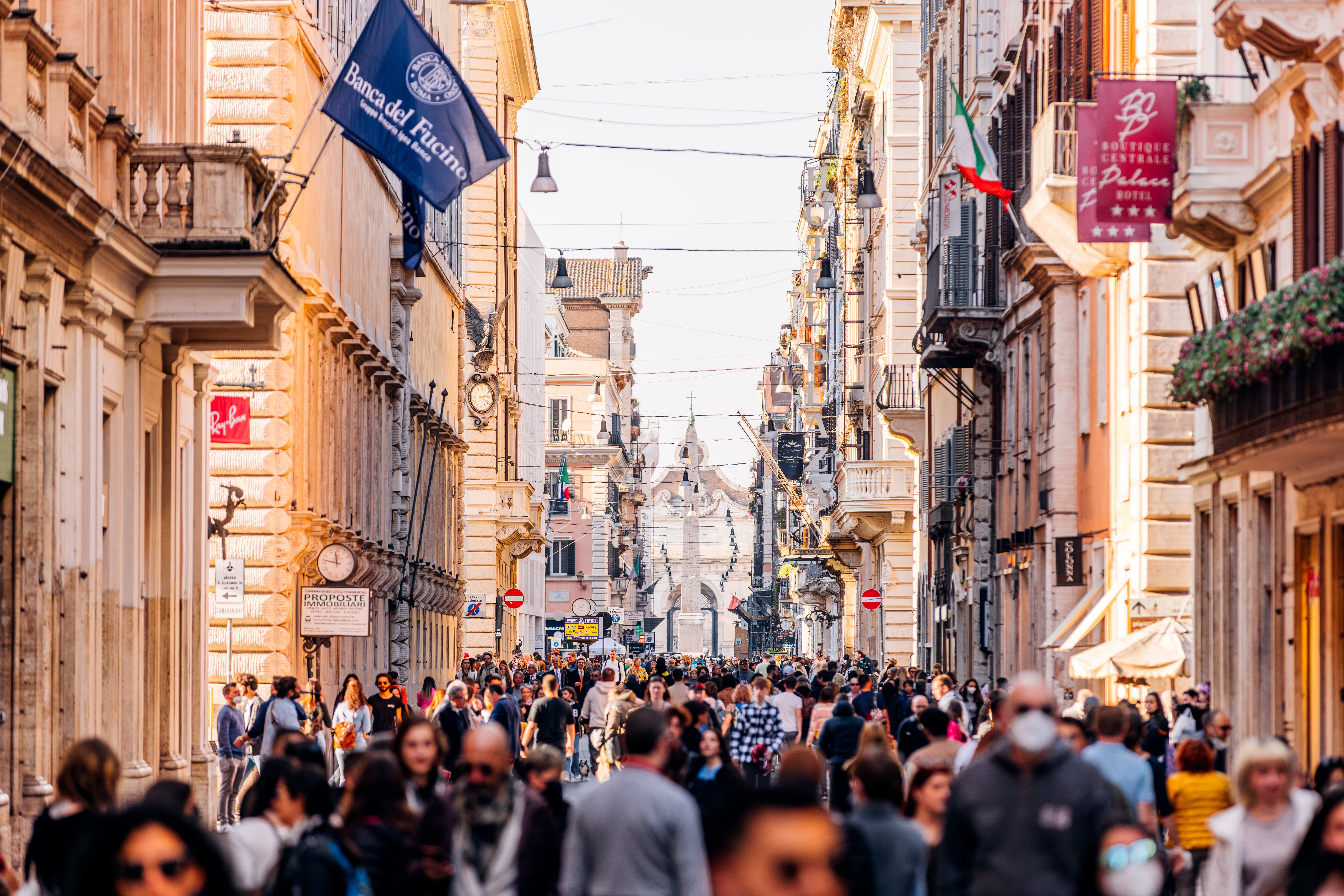 Busy thoroughfare  country   with a assemblage  of radical   walking done  a European city, surrounded by historical  architecture and flags hanging above