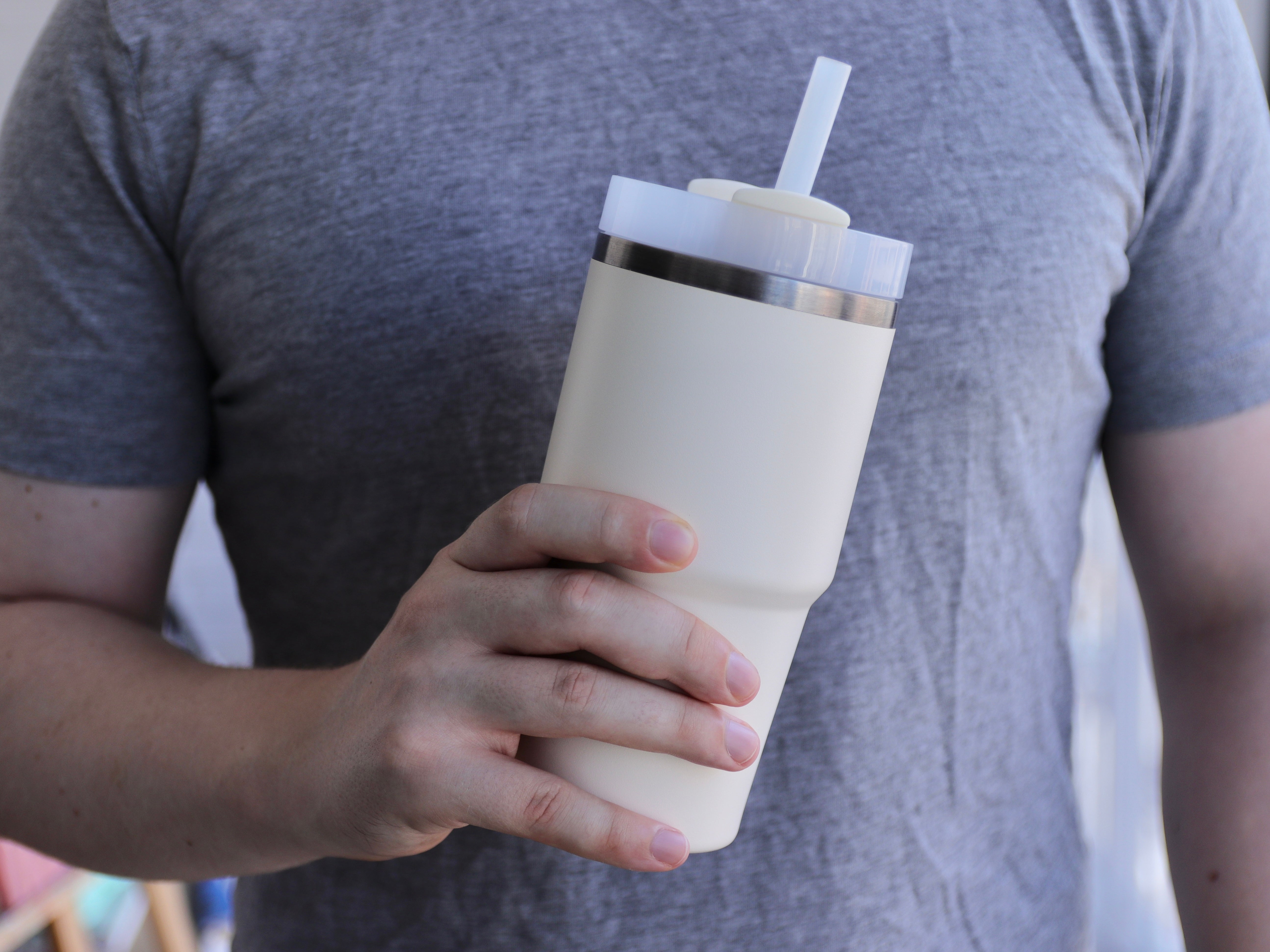 Person holding a reusable tumbler with a straw, wearing a plain t-shirt