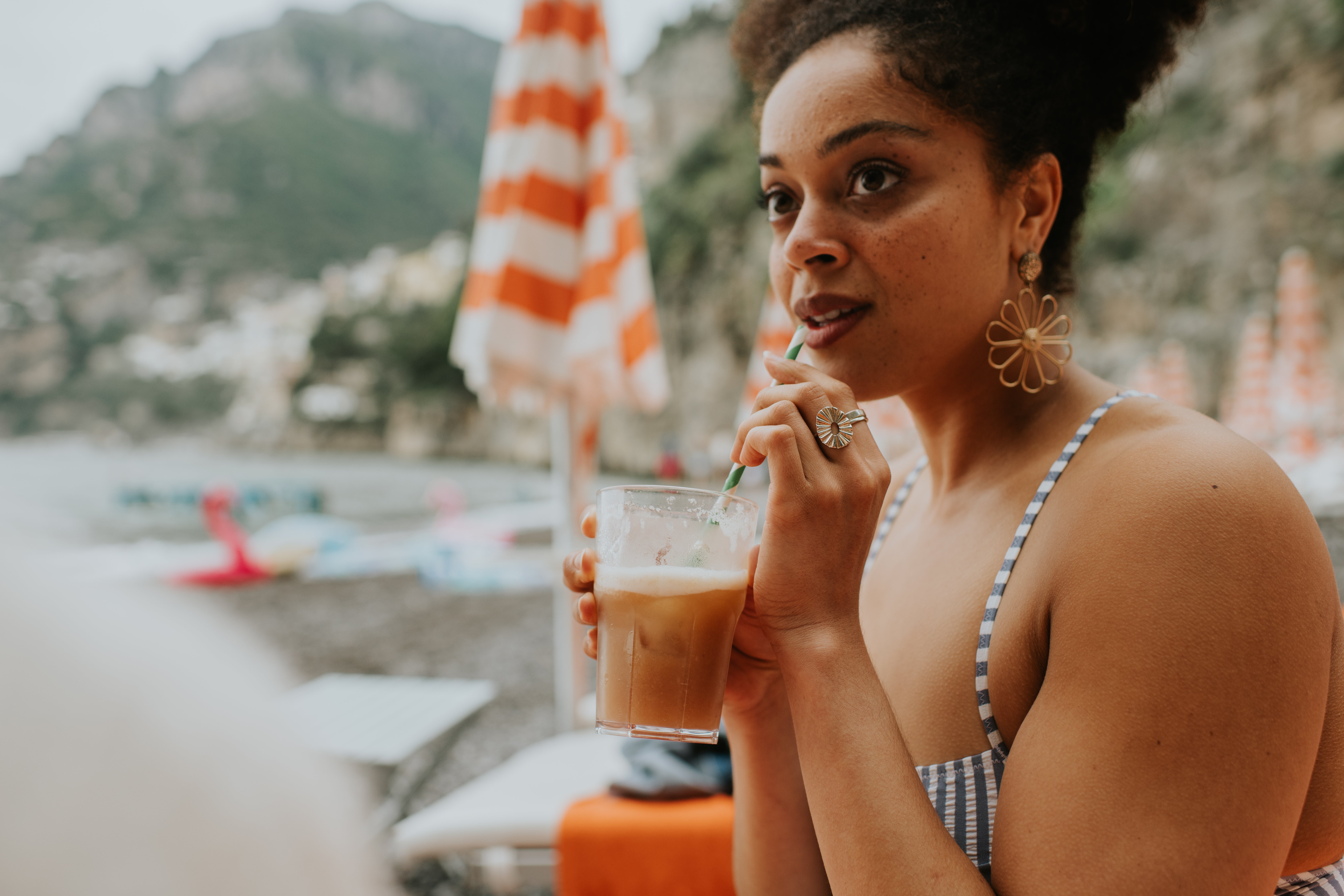 Person successful  a striped swimsuit sips iced portion  connected  a formation  with umbrellas and blurred mountains successful  the background
