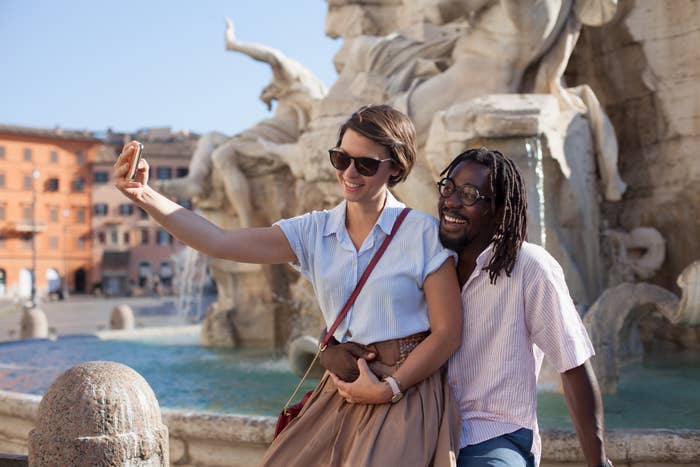 Two radical   smiling and taking a selfie successful  beforehand   of a ample  fountain with sculptures