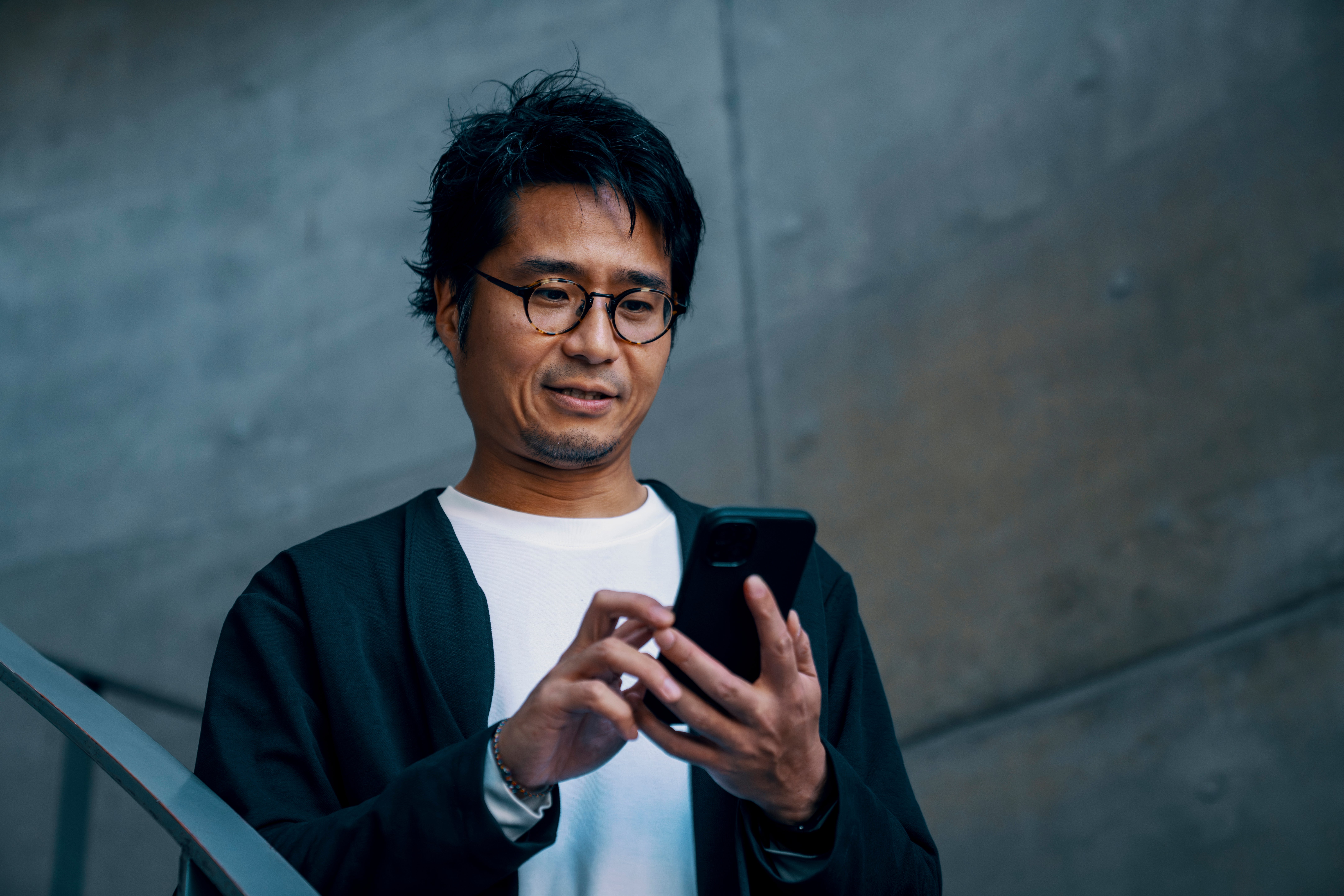 Person successful  a casual unfastened  overgarment   and t-shirt, looking astatine  a smartphone, lasting  against a neutral background
