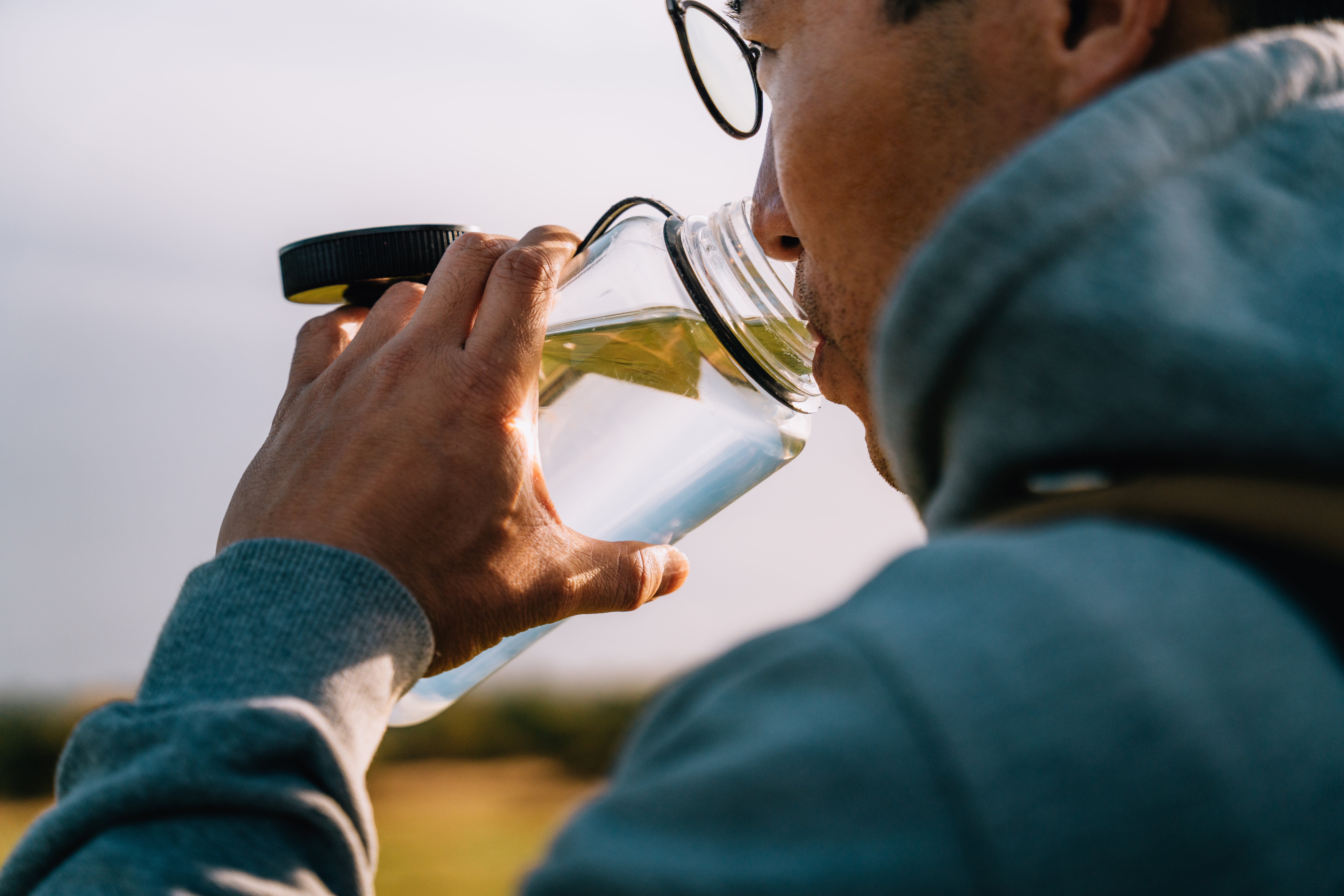 Person successful  glasses drinking from a vessel  outdoors, dressed successful  a hoodie