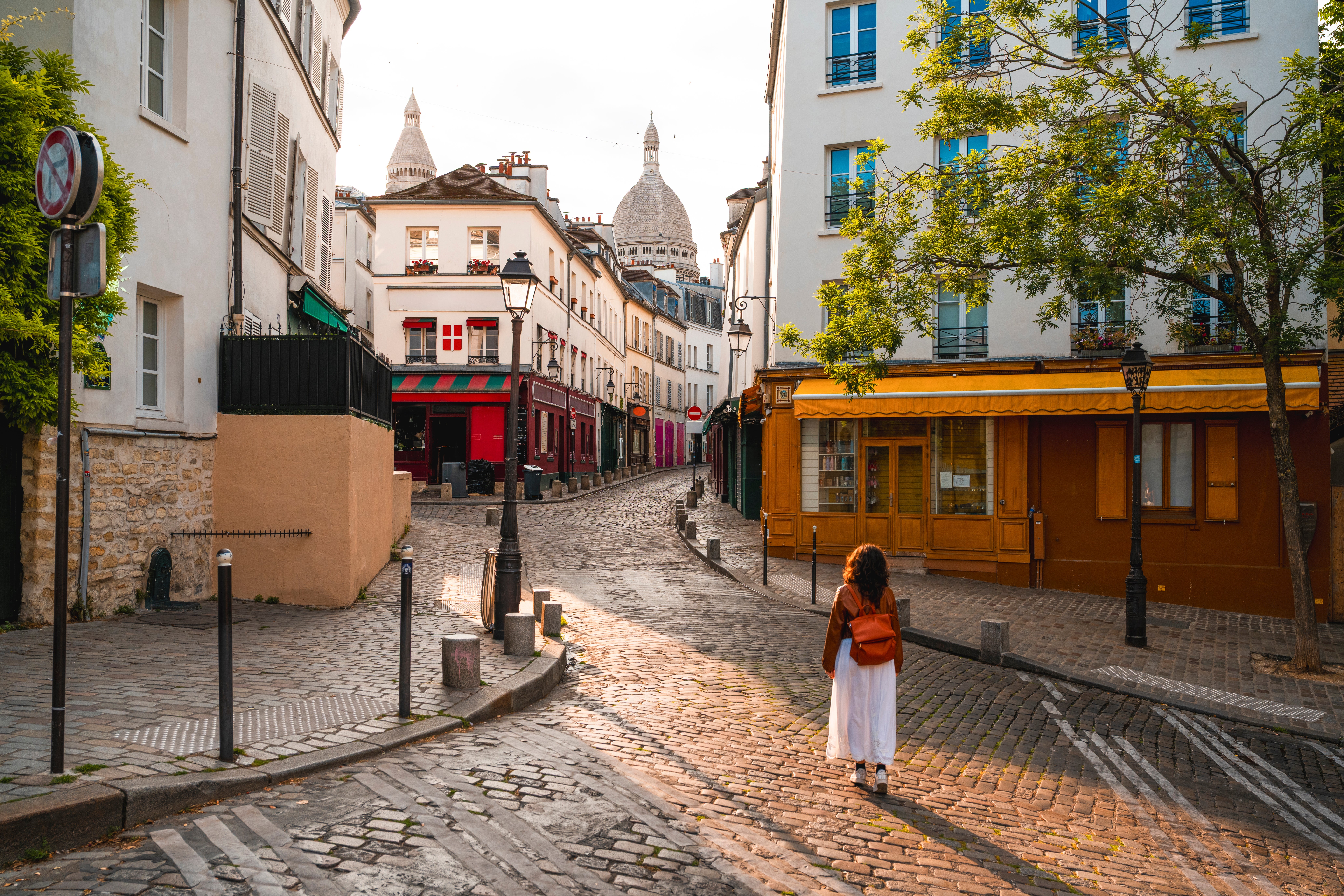 A idiosyncratic   with a backpack walks down   a quaint, cobblestone thoroughfare  successful  a charming European-style neighborhood