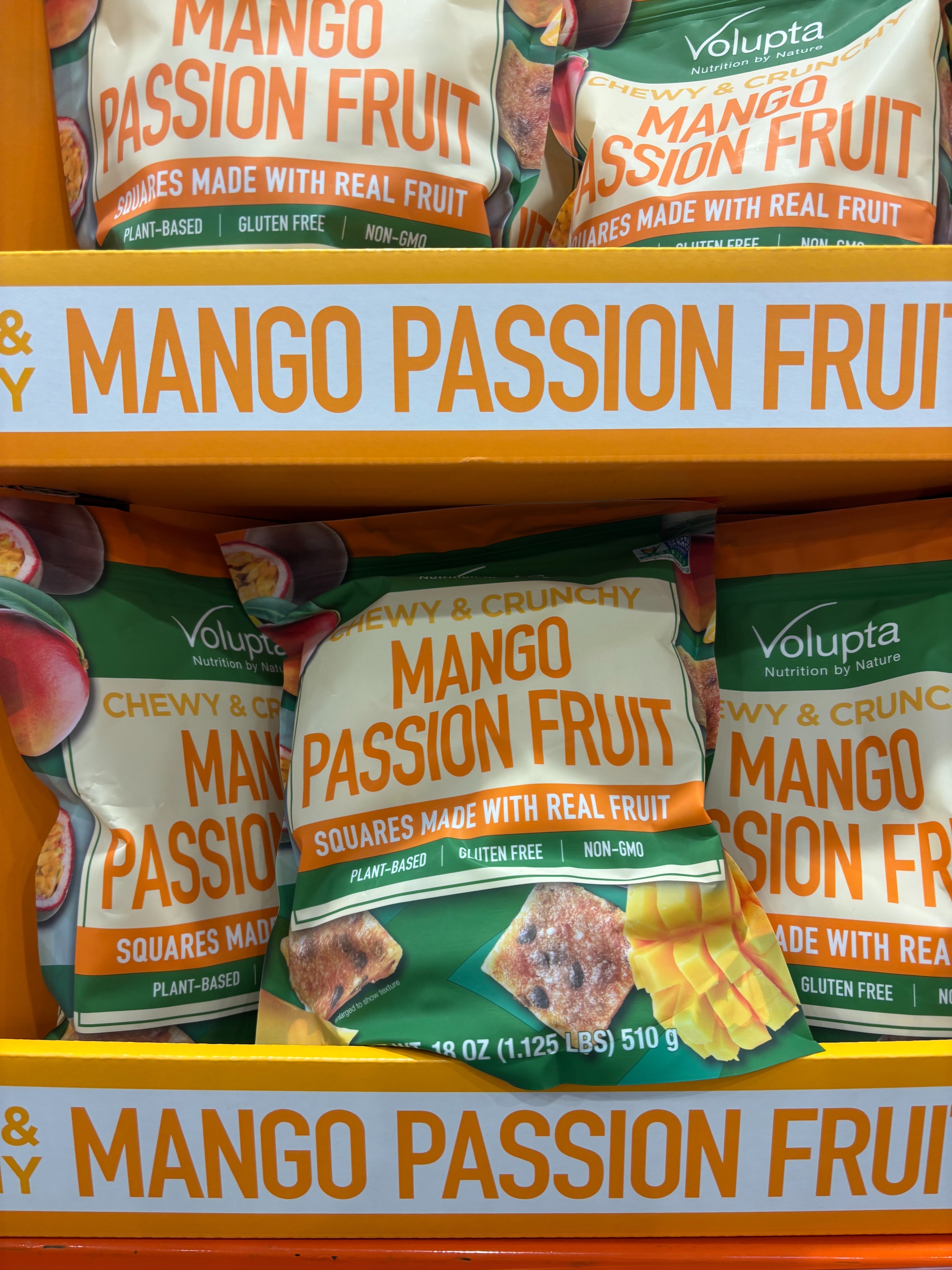 Bags of Volupta Mango Passion Fruit snacks displayed on store shelves, labeled as chewy, crunchy, plant-based, gluten-free, and non-GMO
