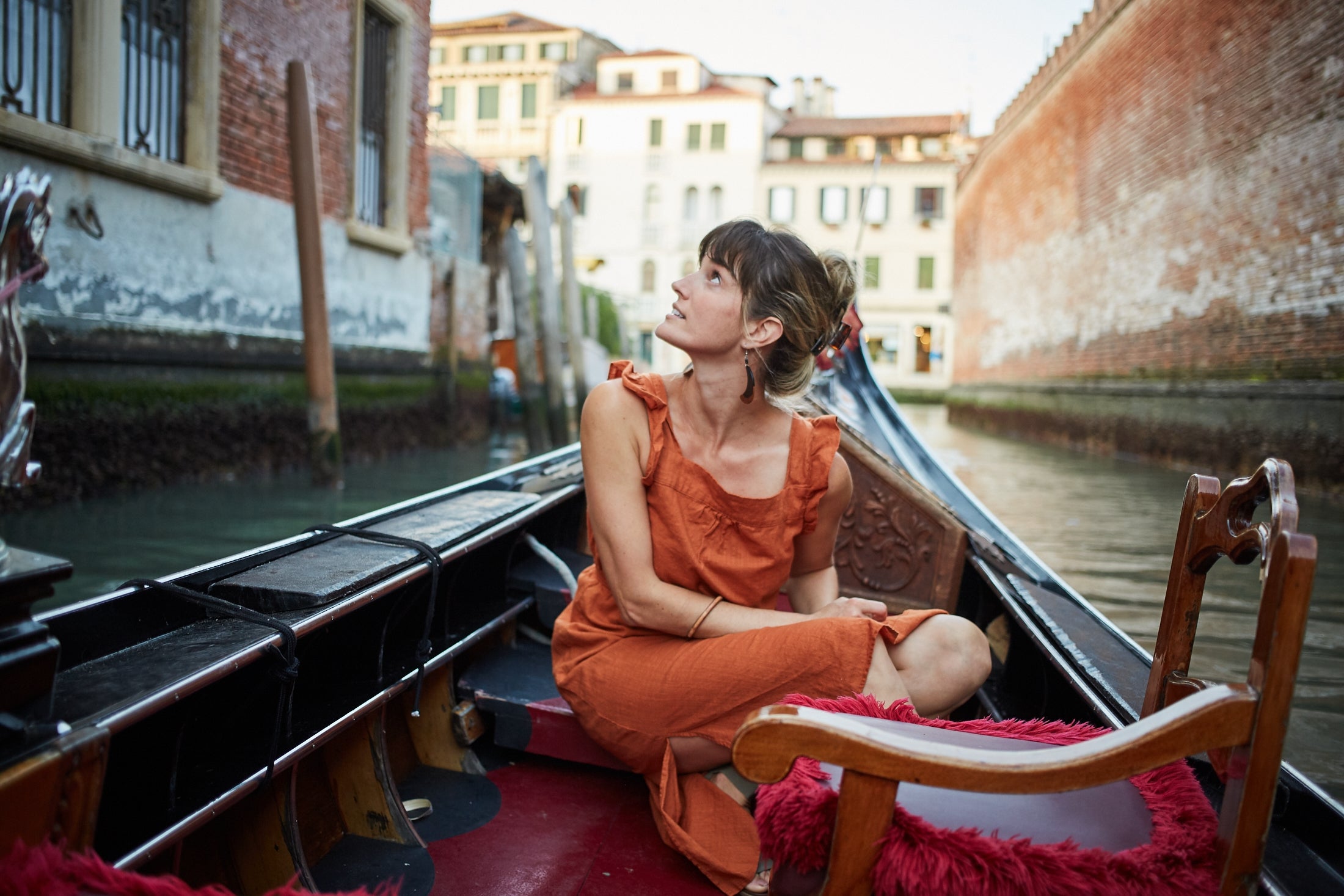 A pistillate   successful  an orangish  formal  sits thoughtfully successful  a gondola, navigating a canal successful  a historical  metropolis  setting