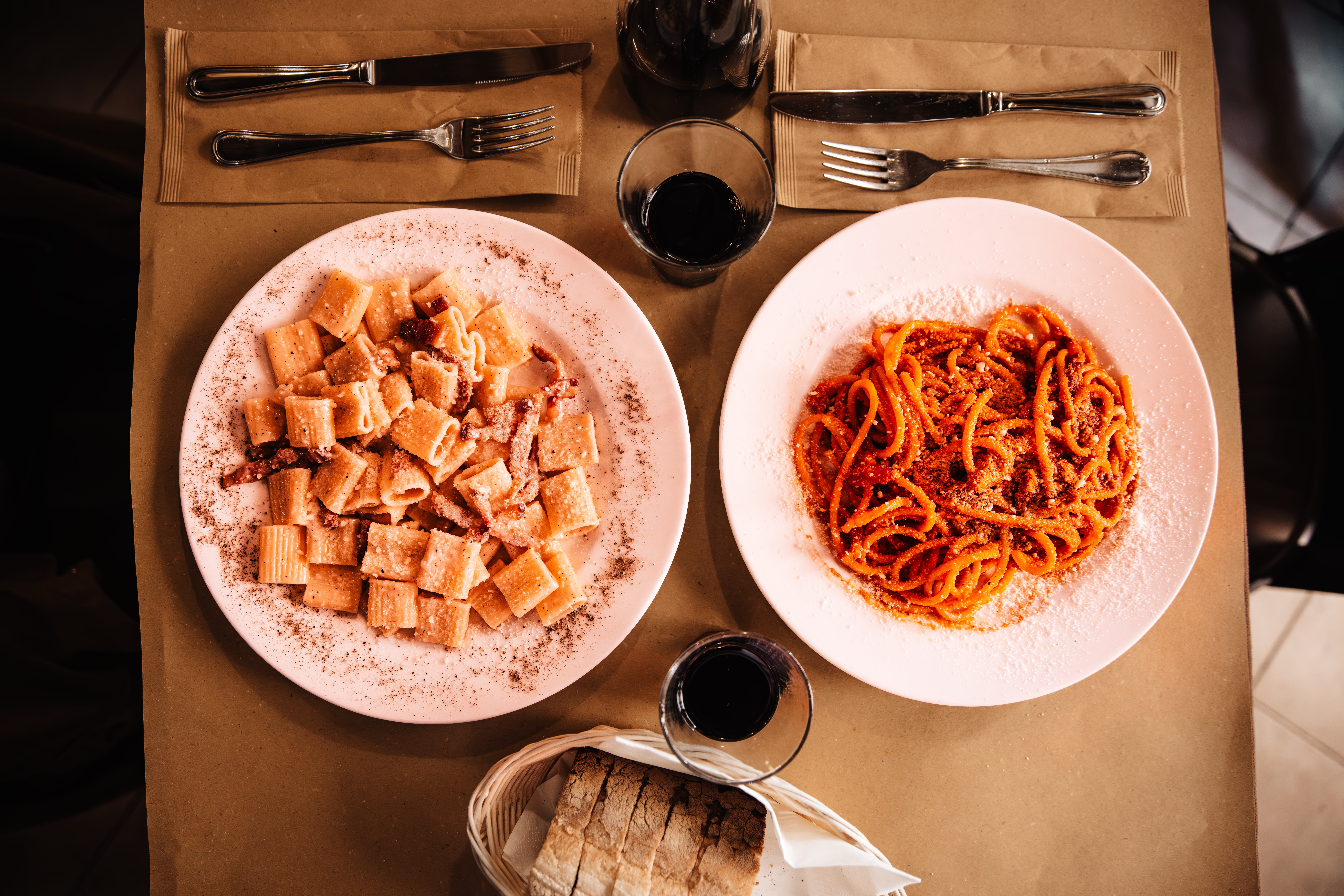 Two plates of pasta, 1  with rigatoni successful  pick  sauce, the different   with spaghetti successful  reddish  sauce, are acceptable   connected  a array  with drinks and bread