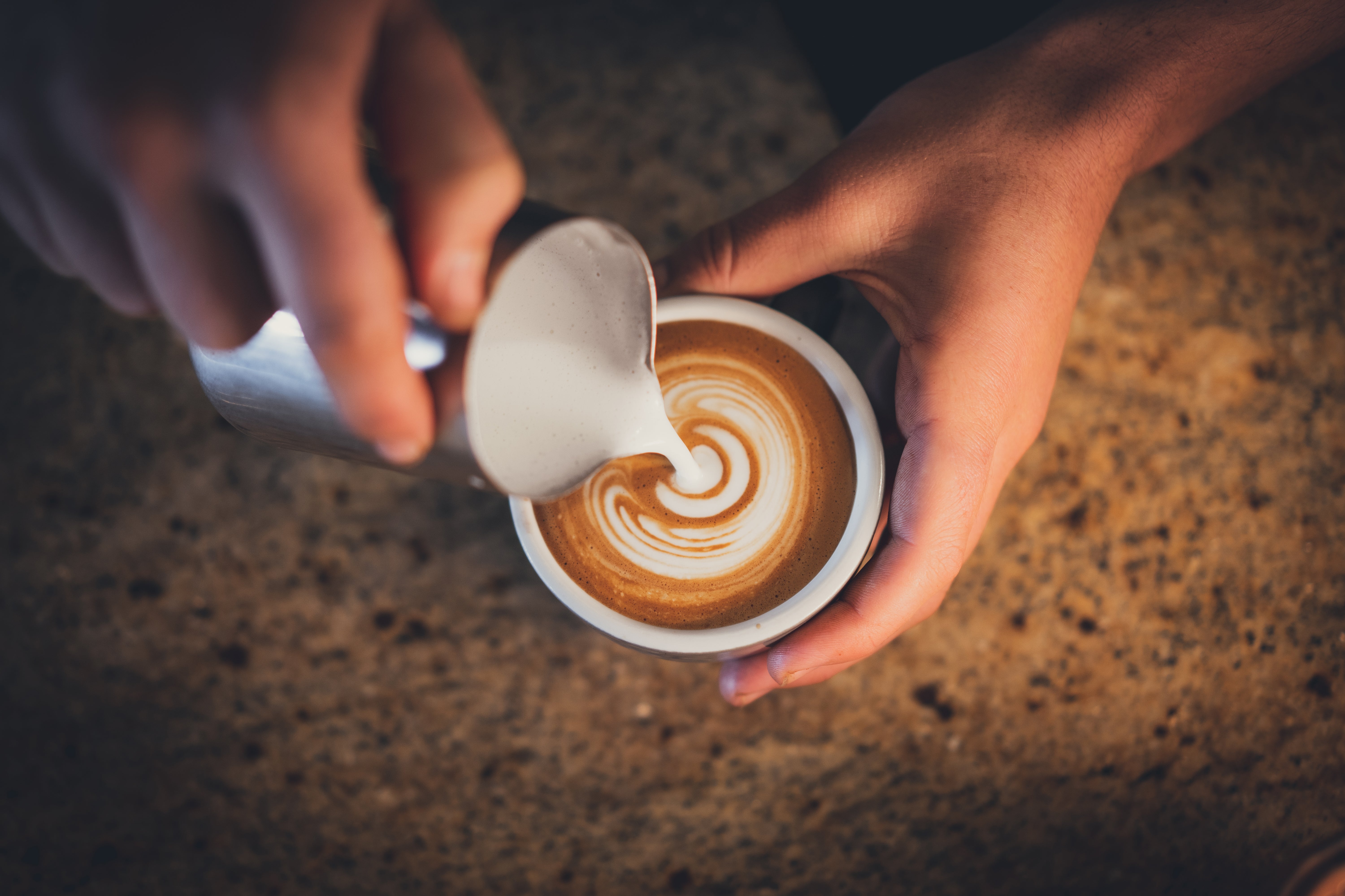 Person pouring beverage  creating latte creation  successful  a java  cupful  connected  a woody  table