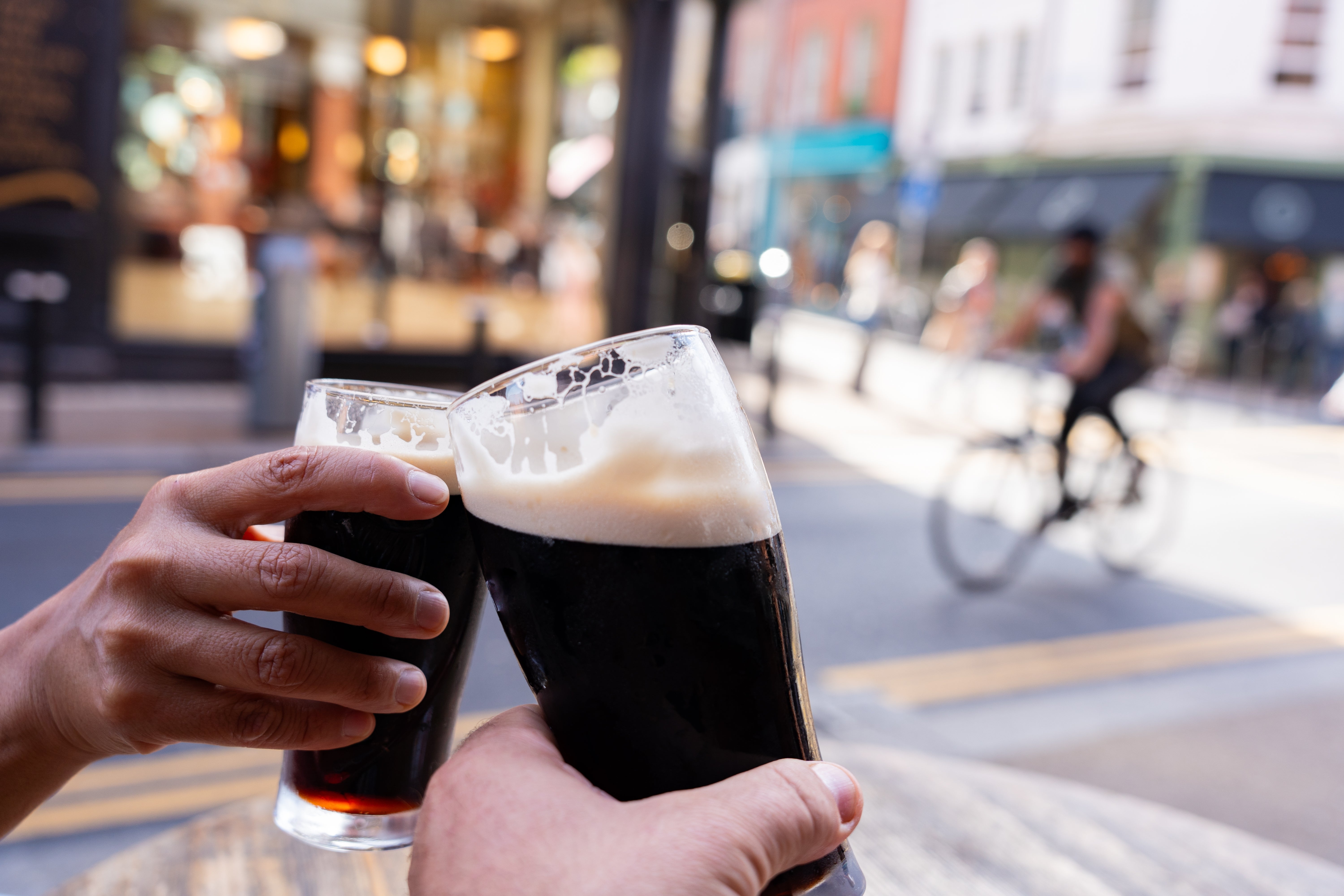 Two radical   clink glasses of acheronian  brew  outside, with a cyclist successful  the inheritance  connected  a metropolis  street