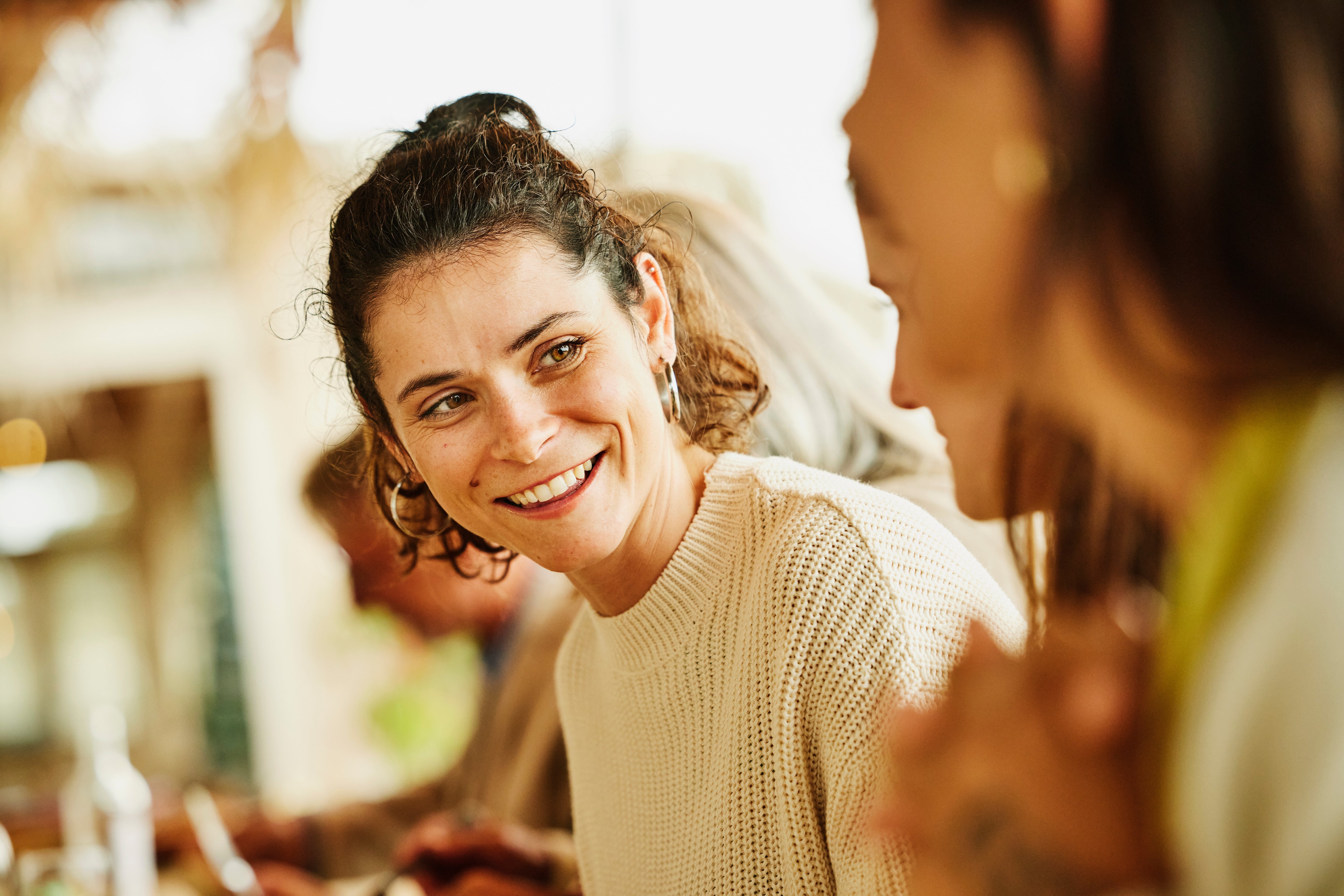 Person smiling warmly, wearing a textured sweater, engaging with different  idiosyncratic   successful  a casual setting. Blurred inheritance  with others around