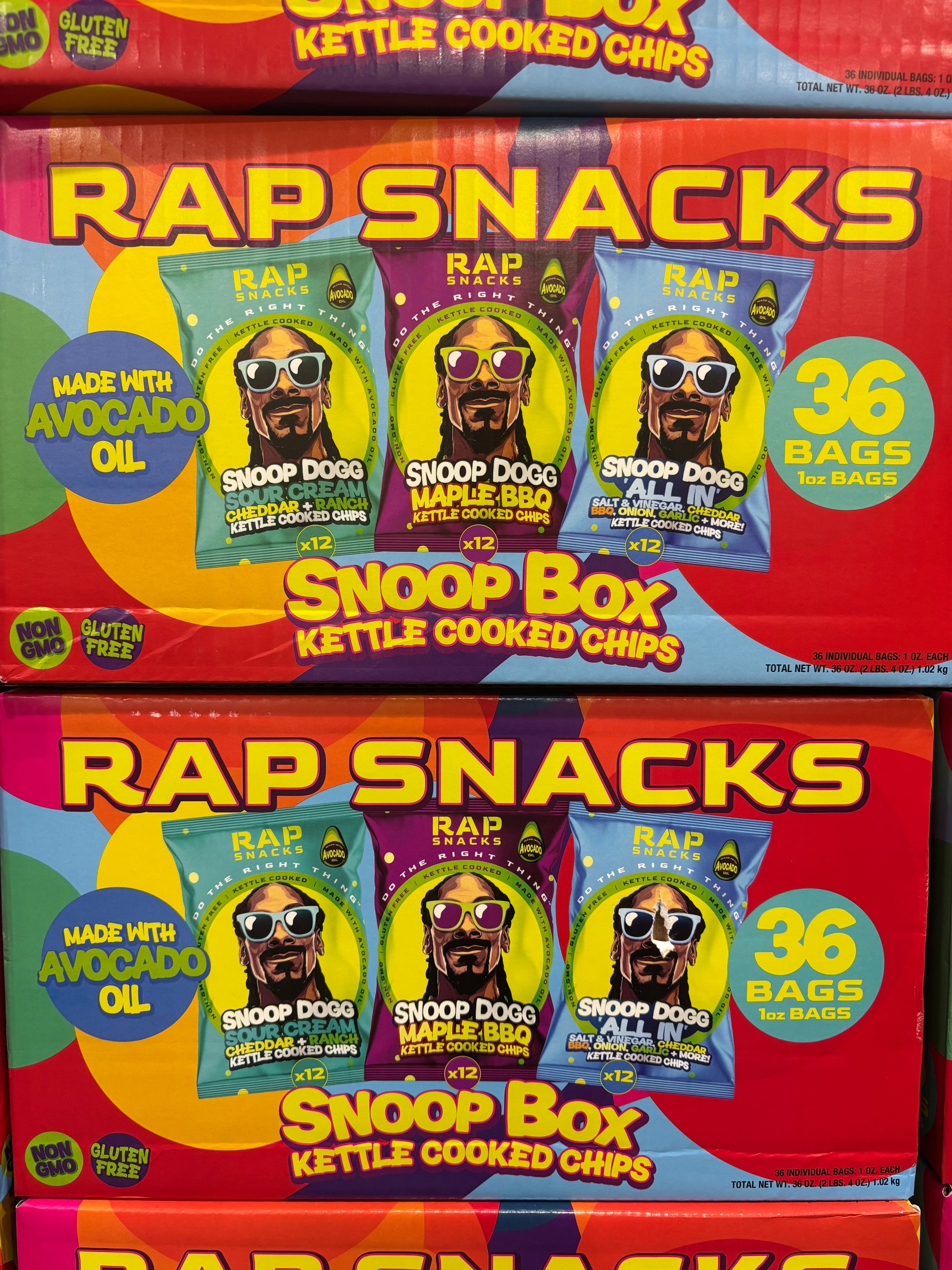 Boxes of Rap Snacks featuring Snoop Dogg on the front, labeled as "Snoop Box Kettle Cooked Chips." Made with avocado oil, 36 bags per box