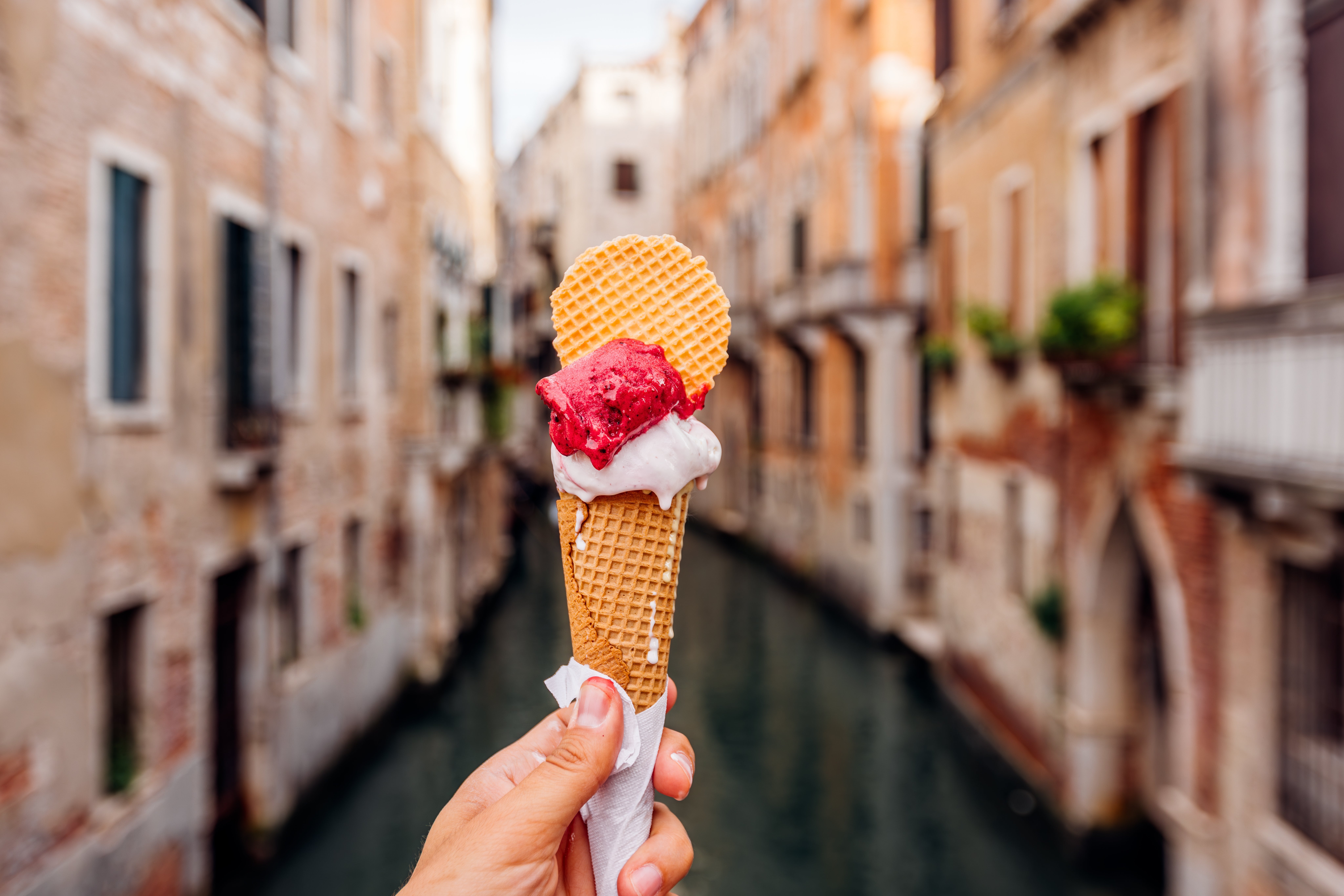 Hand holding an crystal  pick  cone with waffle and strawberry scoop successful  beforehand   of a canal view, apt  successful  Venice