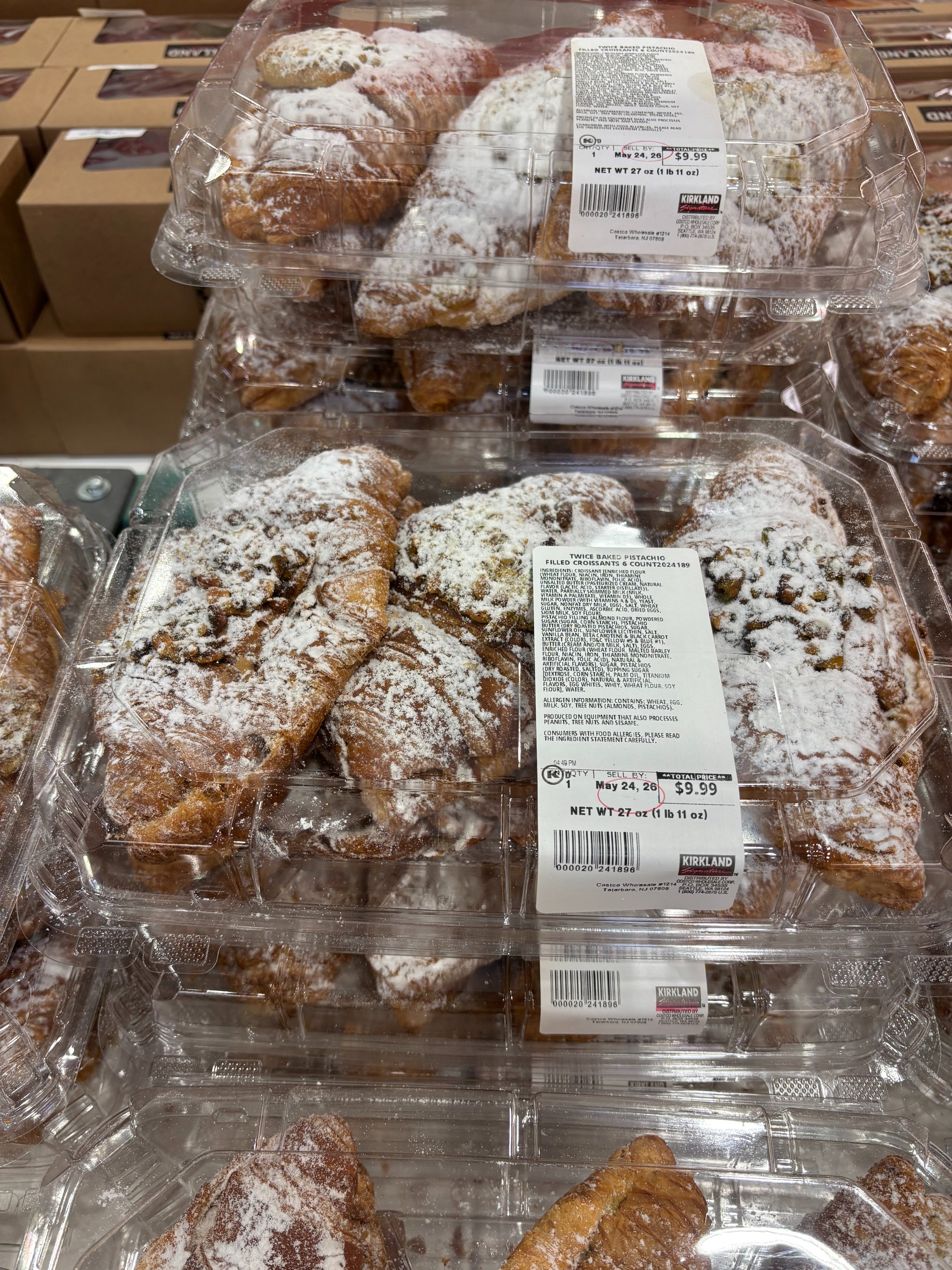 Stacks of croissants in plastic packaging on a store shelf, sprinkled with powdered sugar and labeled with pricing and nutritional information