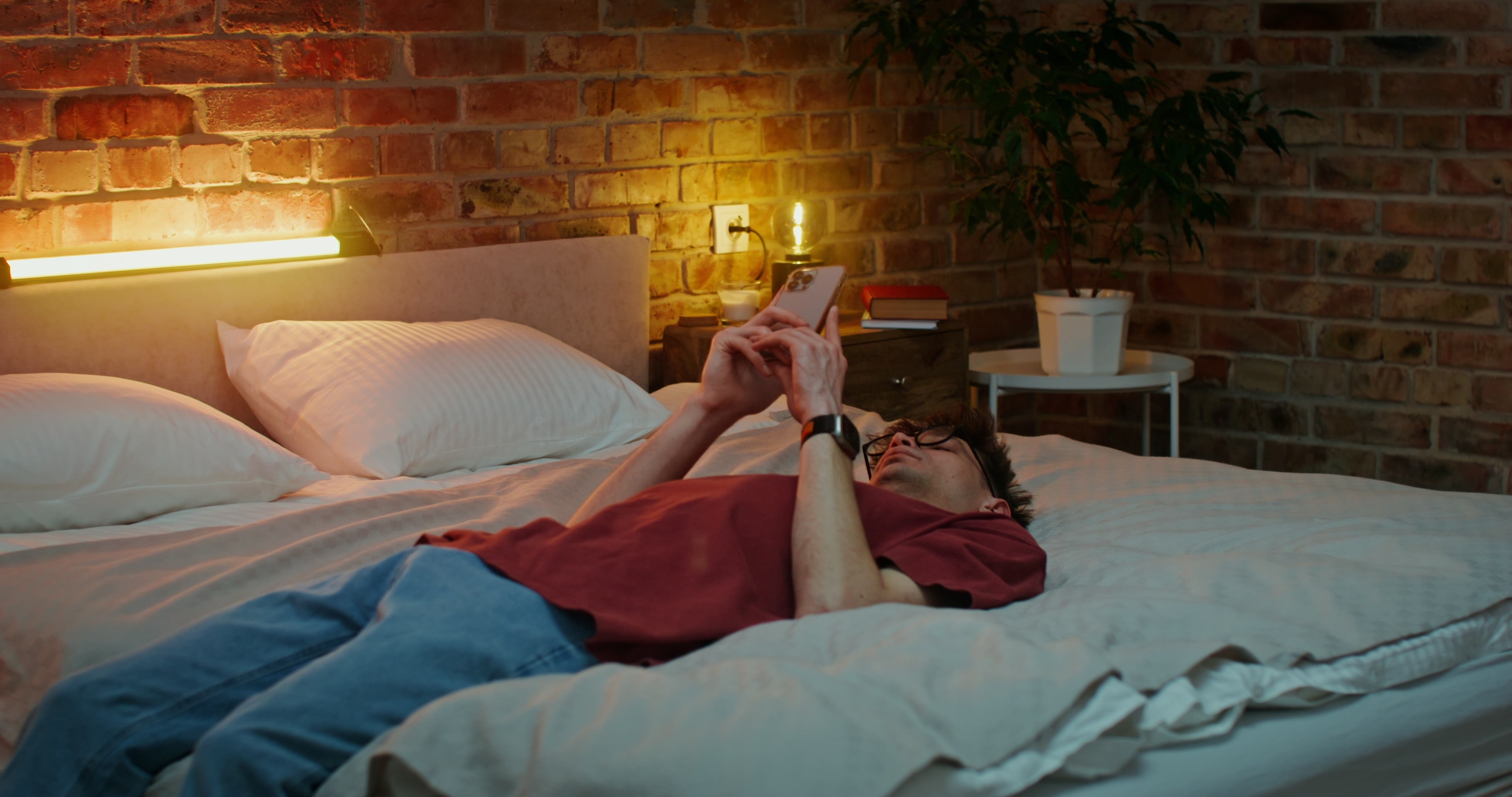 Person som ligger på en seng i et koselig rom og ser på telefonen med et avslappet uttrykk