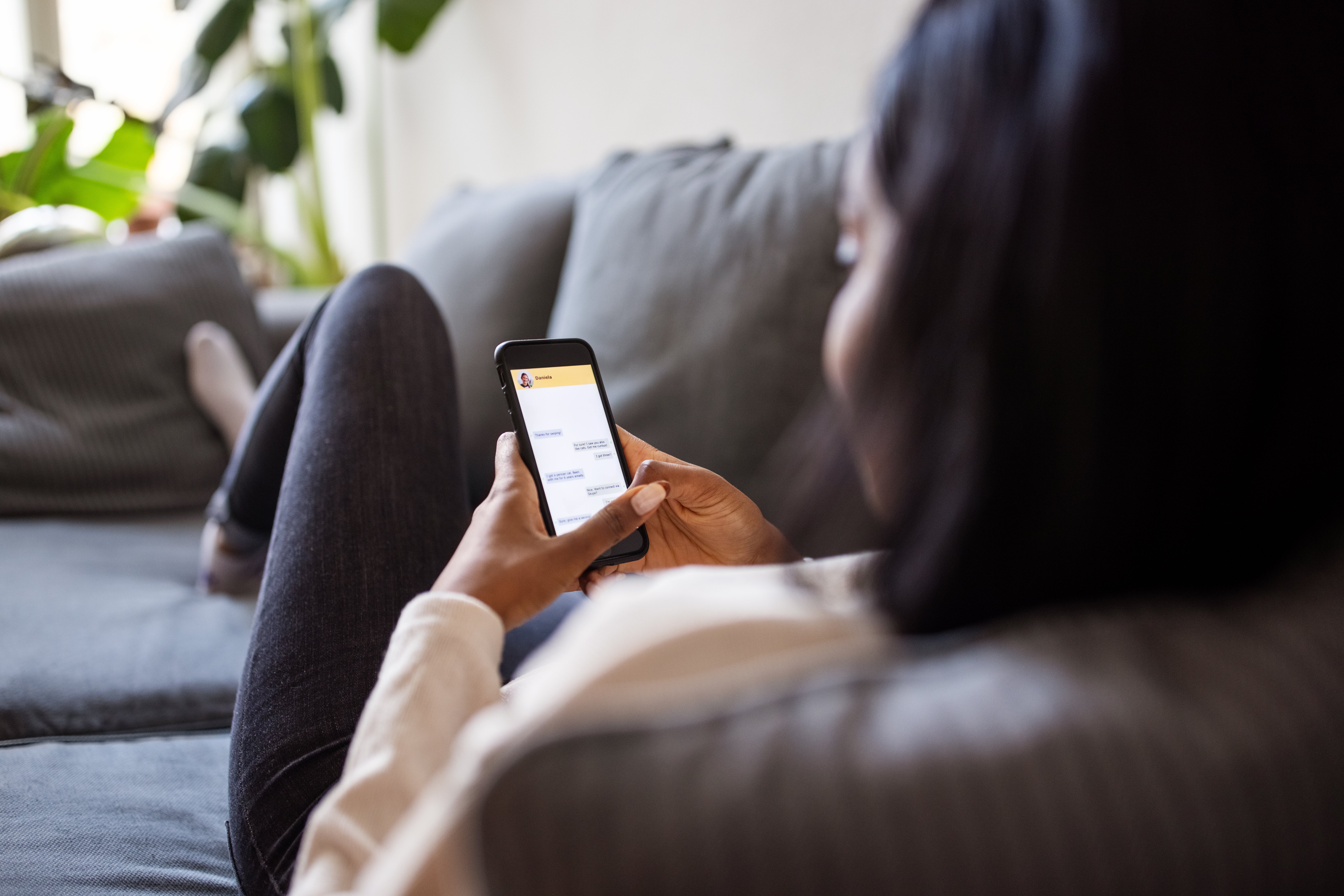 Person som slapper av på en sofa, fokusert på å sende tekstmeldinger på smarttelefonen, og foreslår et tilfeldig og intimt kommunikasjonsøyeblikk