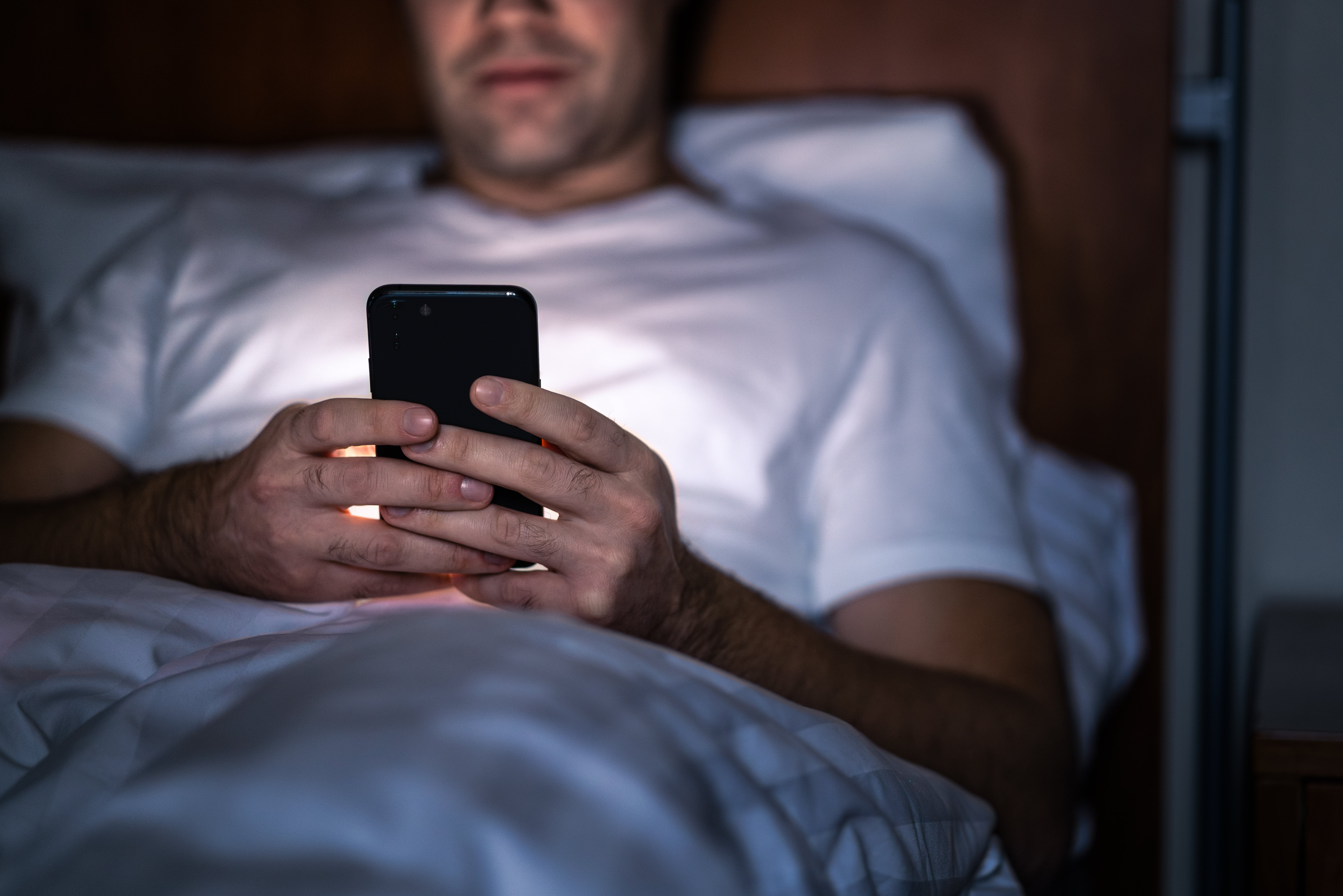 Person som ligger i sengen om natten, fokusert på smarttelefonen sin, og foreslår et privat eller intimt øyeblikk