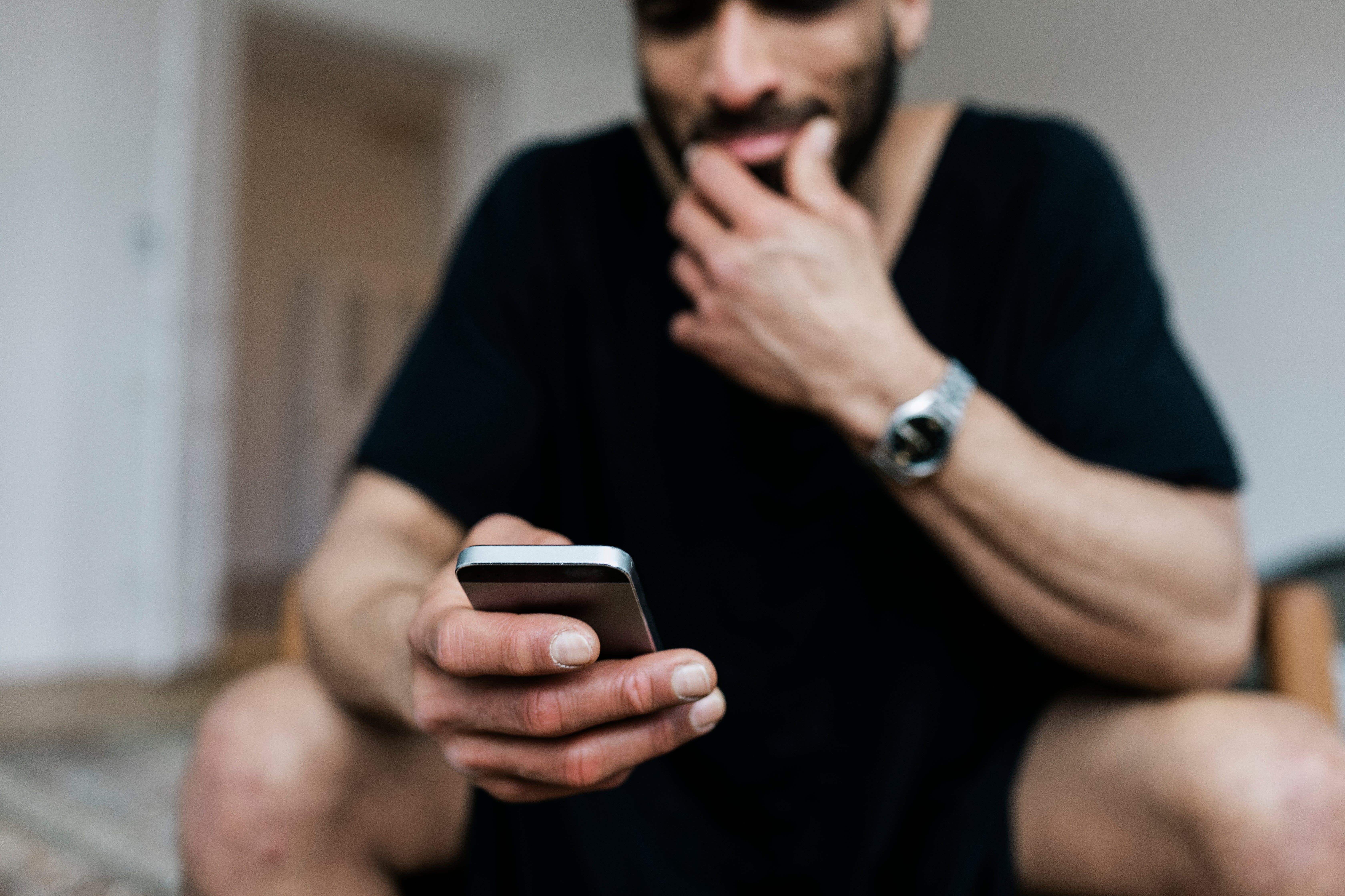 Mann som sitter tilfeldig og holder en smarttelefon, virker gjennomtenkt. Fokus på telefonen antyder engasjement med en melding eller surfing