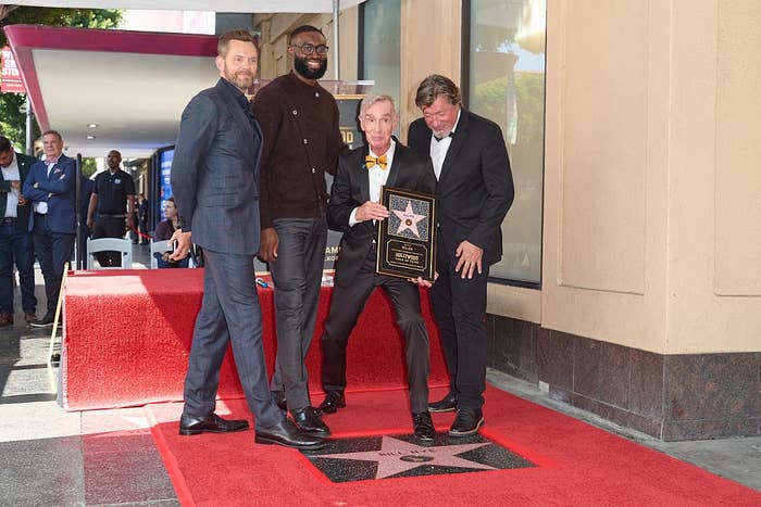 Four people pose with a Hollywood Walk of Fame star plaque. One holds the plaque, smiling, as the others stand nearby on the red carpet