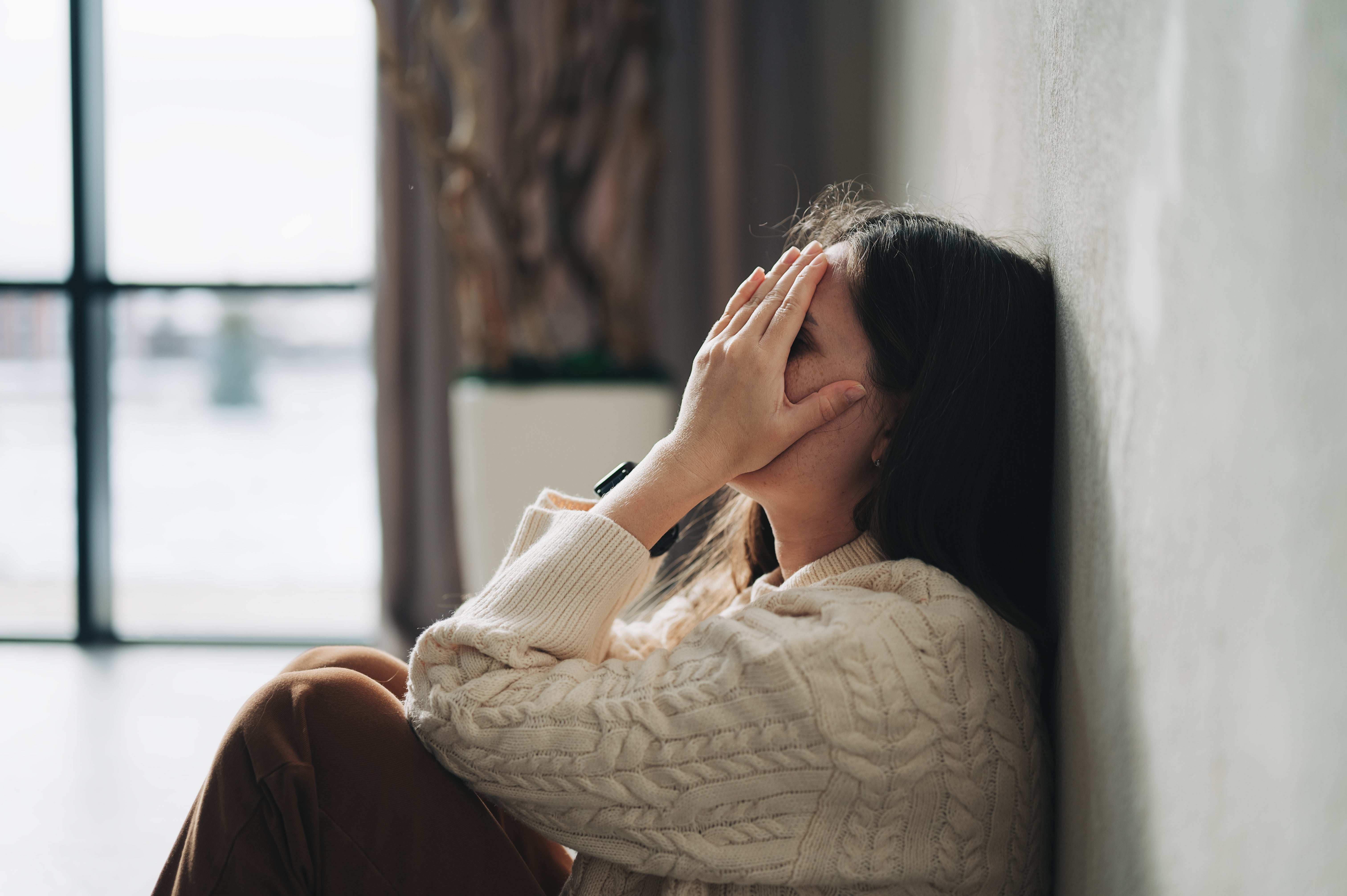 A idiosyncratic sits against a wall, look successful hands, appearing distressed oregon heavy successful thought. They deterioration a knitted sweater