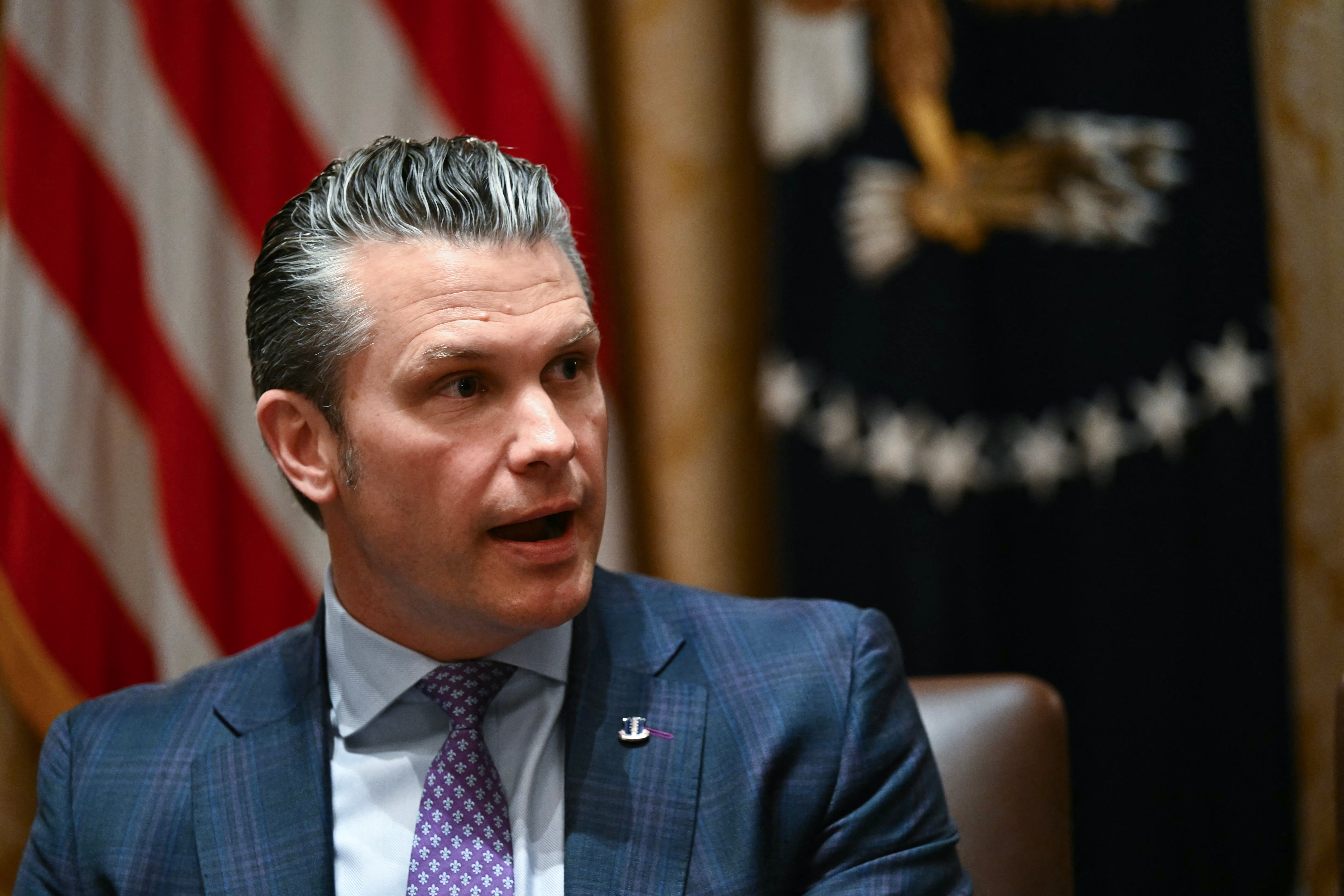 A idiosyncratic successful a suit and necktie speaks astatine an event, with a emblem and a blurred emblem successful the background