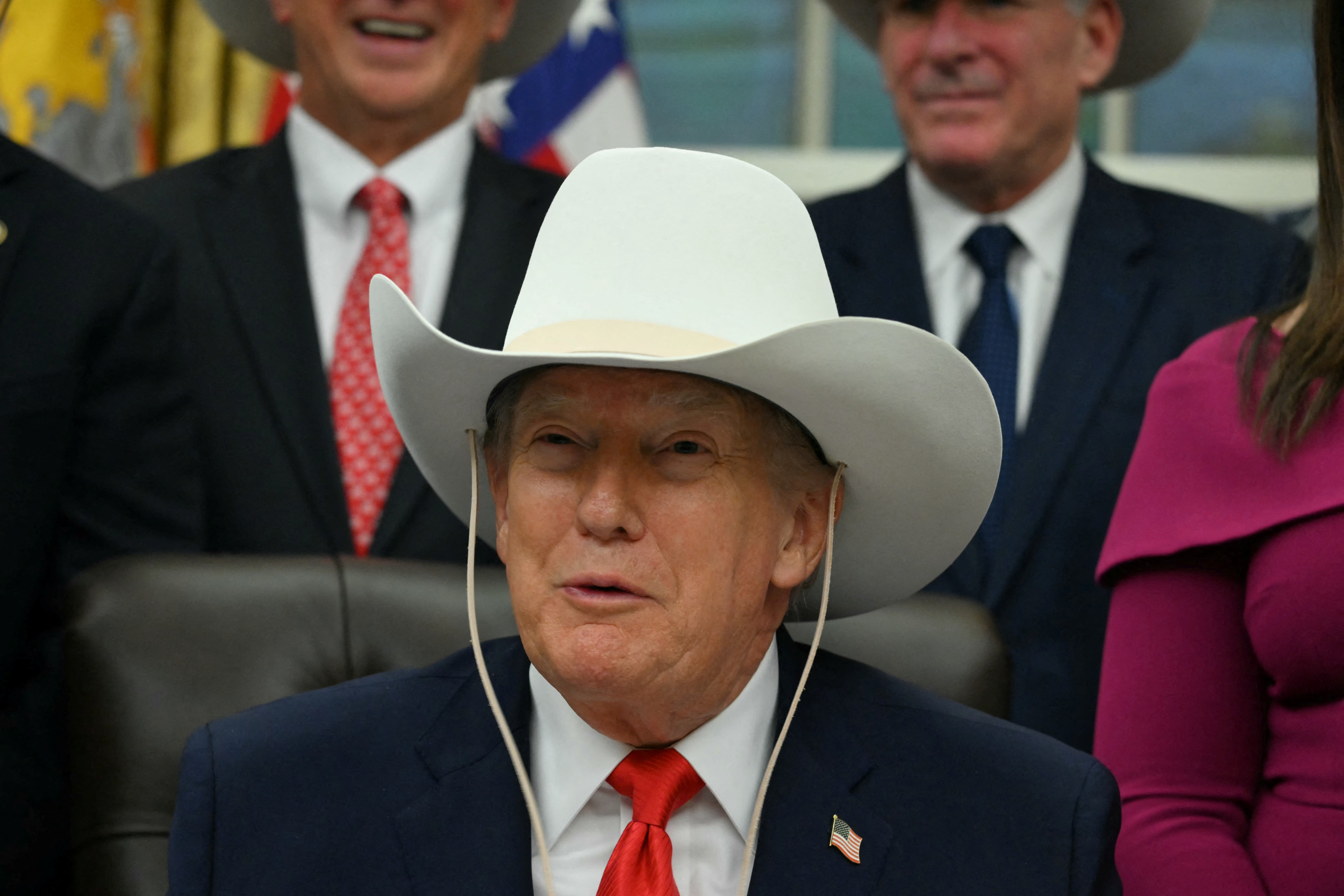 Person successful a suit and achromatic cowboy chapeau speaking astatine an event, surrounded by others successful suits